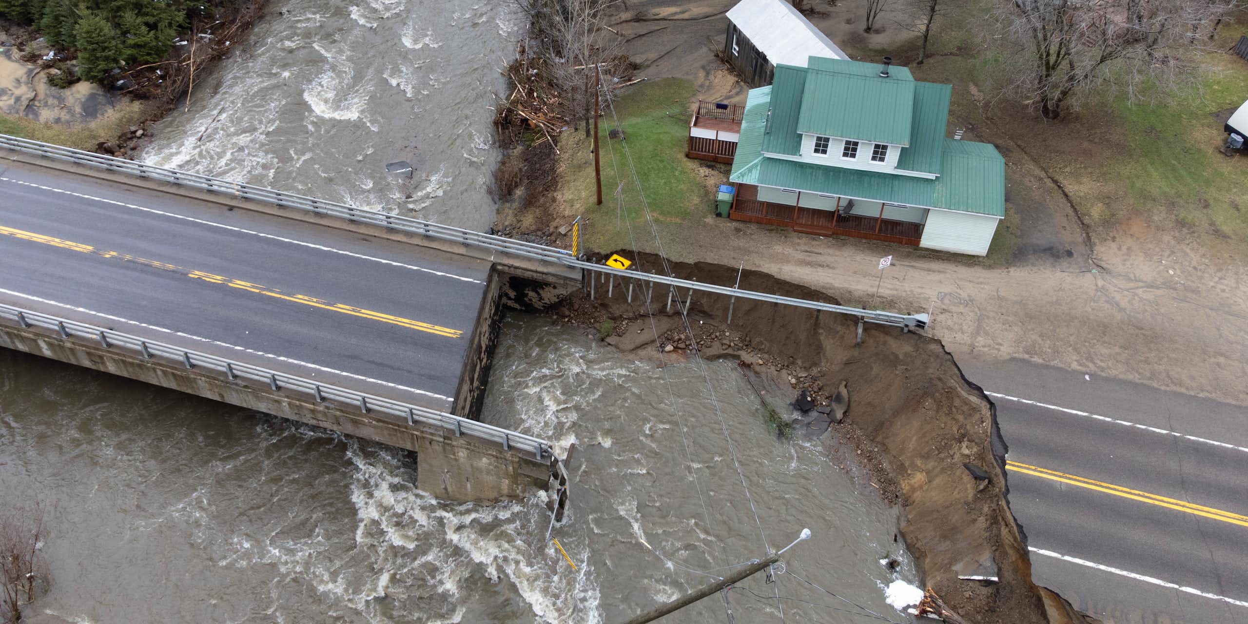 Vue aérienne d'une zone inondée, avec une route coupée en deux, et une maison au toit vert en arrière-plan