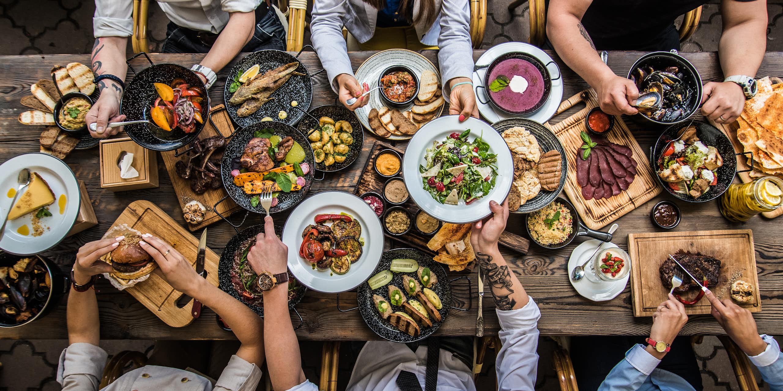 Vue de haut d'une tablée composée d'aliments divers, avec des gens attablés tout autour