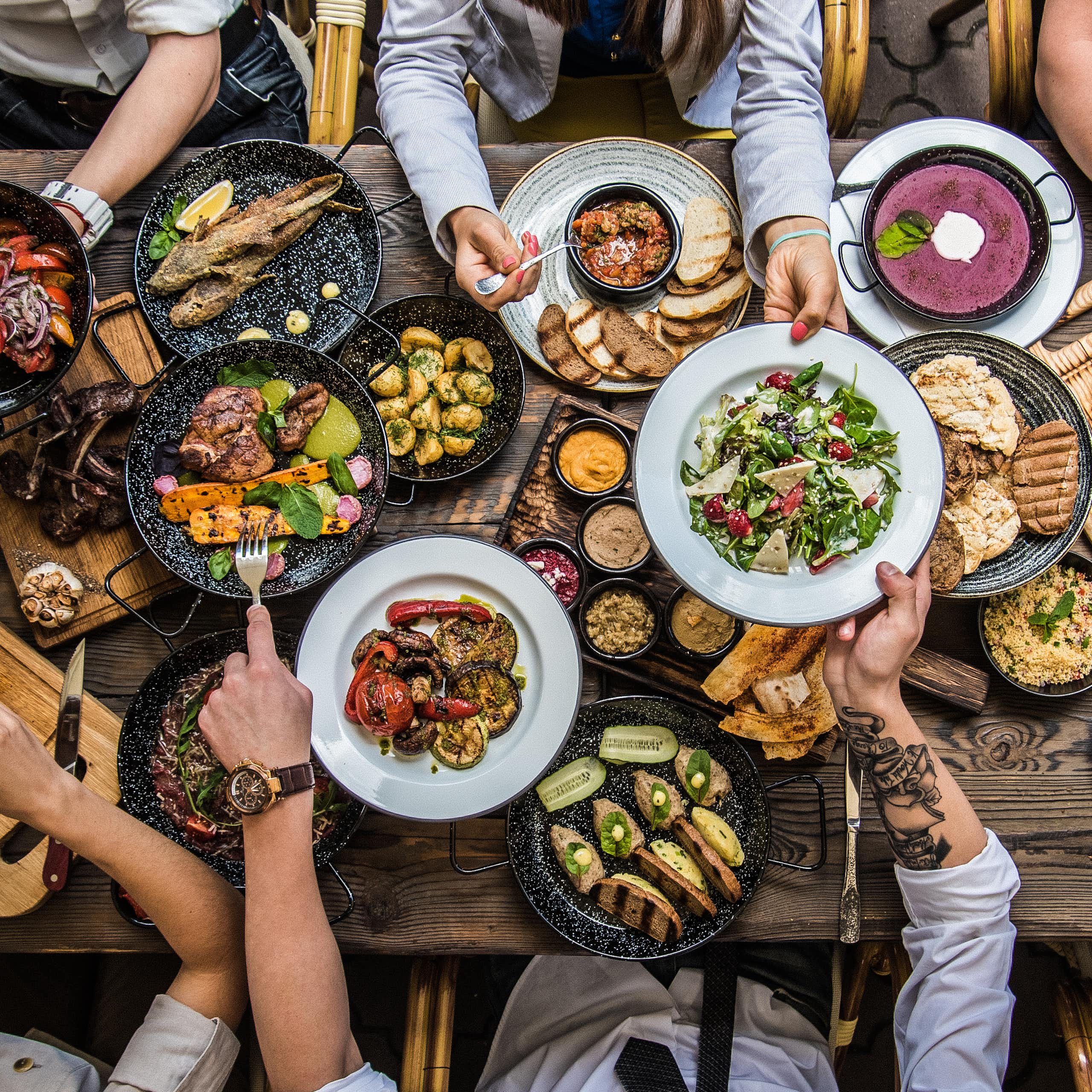 Vue de haut d'une tablée composée d'aliments divers, avec des gens attablés tout autour