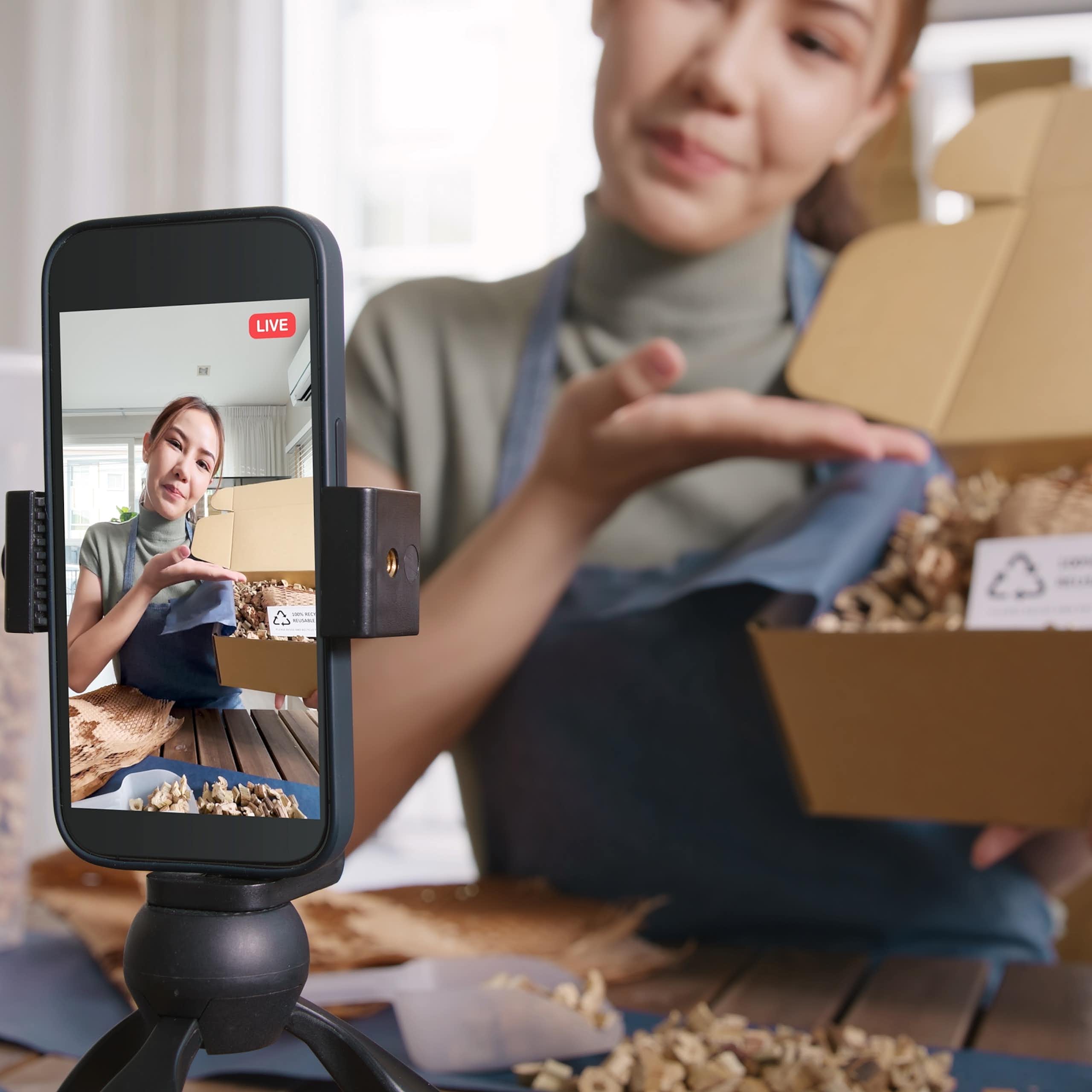 Une femme présente le contenu d'une boîte devant un téléphone intelligent