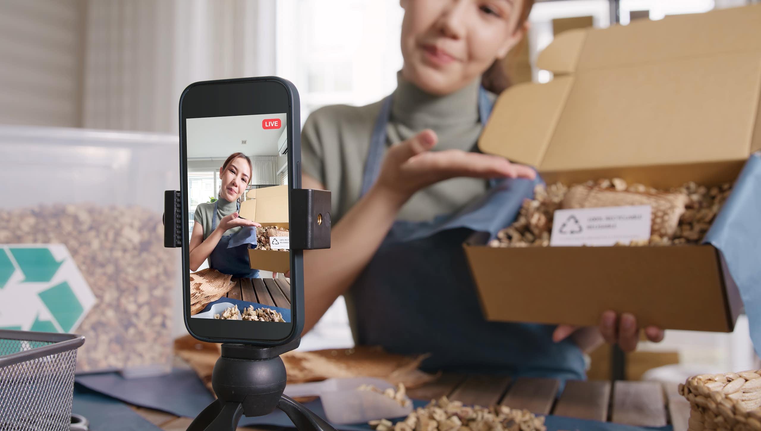 Une femme présente le contenu d'une boîte devant un téléphone intelligent