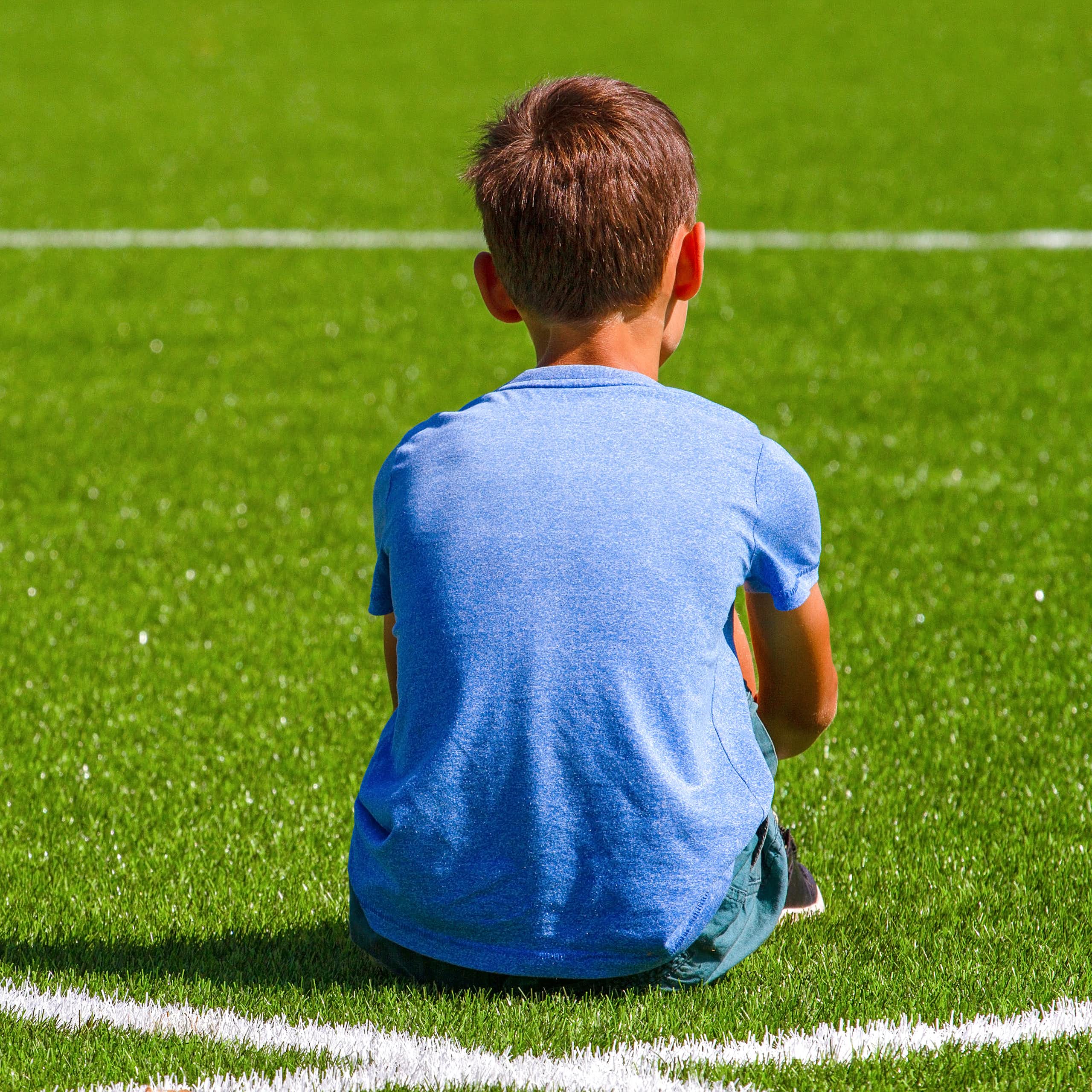 Young boy sitting with his back to a sports field