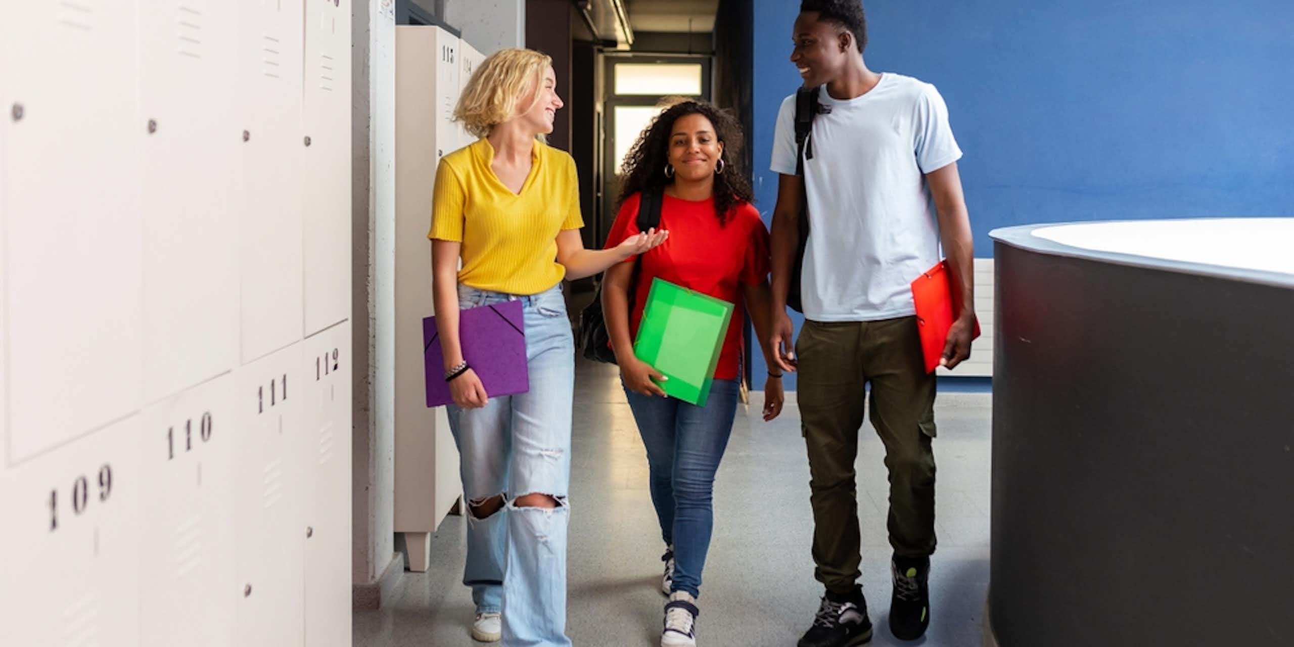 Three young people talking to each other as they walk past some lockers