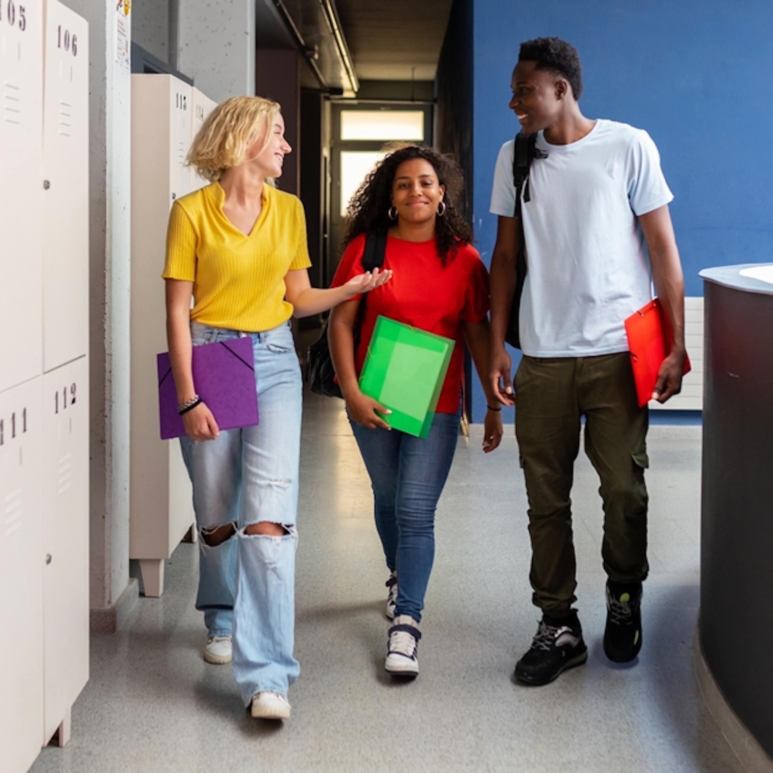 Three young people talking to each other as they walk past some lockers
