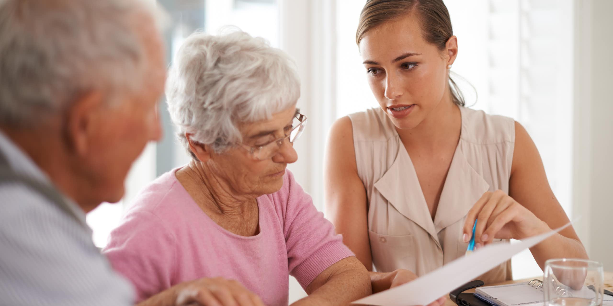 Elderly man and woman being shown a document by a younger woman