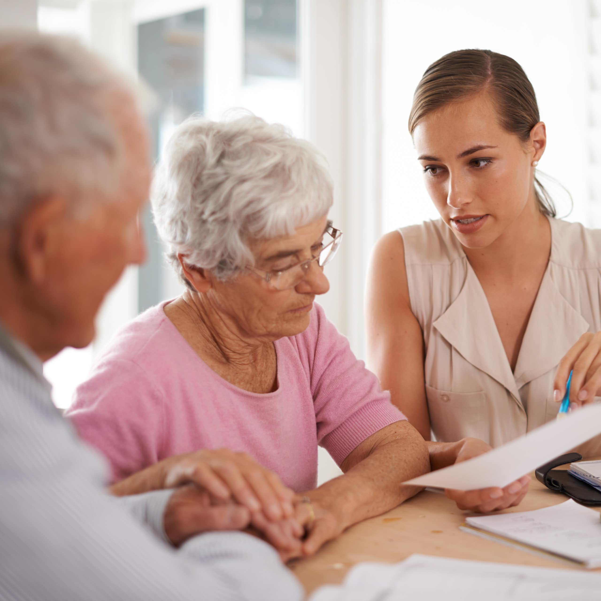 Elderly man and woman being shown a document by a younger woman
