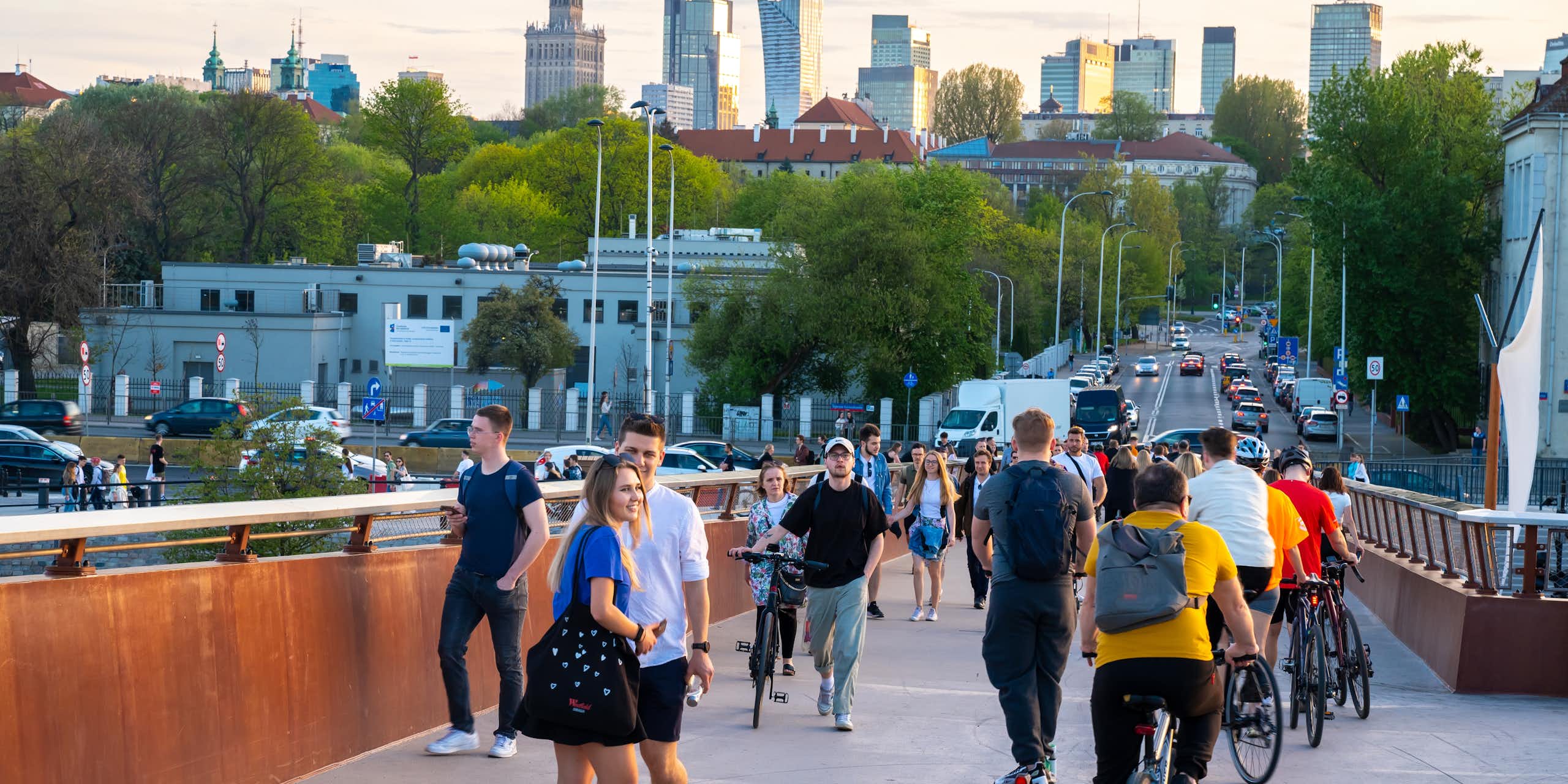 Un groupe de personnes, certaines à vélo, traversent un pont, avec des gratte-ciel à l'arrière-plan.