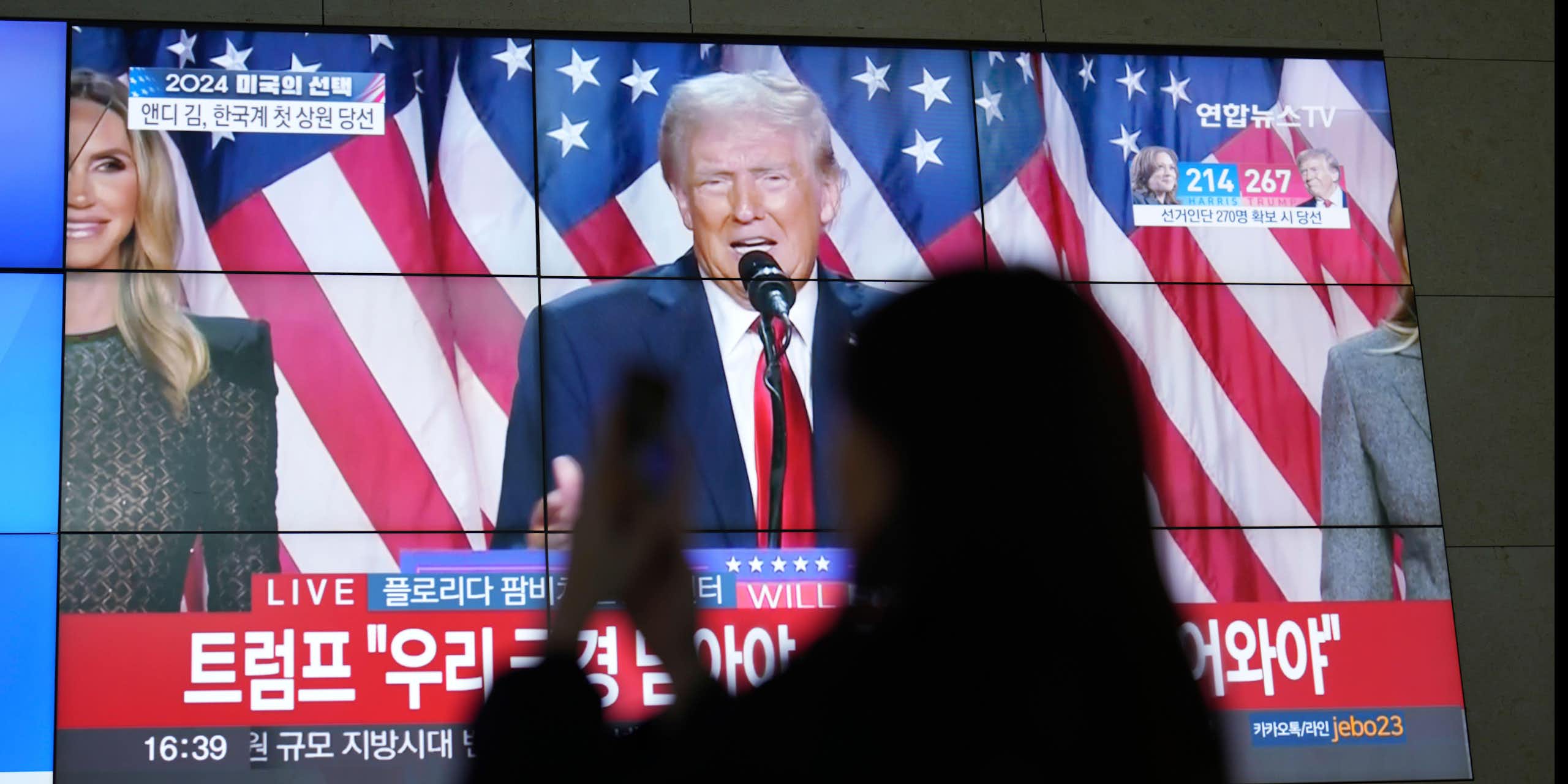 A silhouette of a woman looking at her phone with Donald Trump on a TV screen behind her.