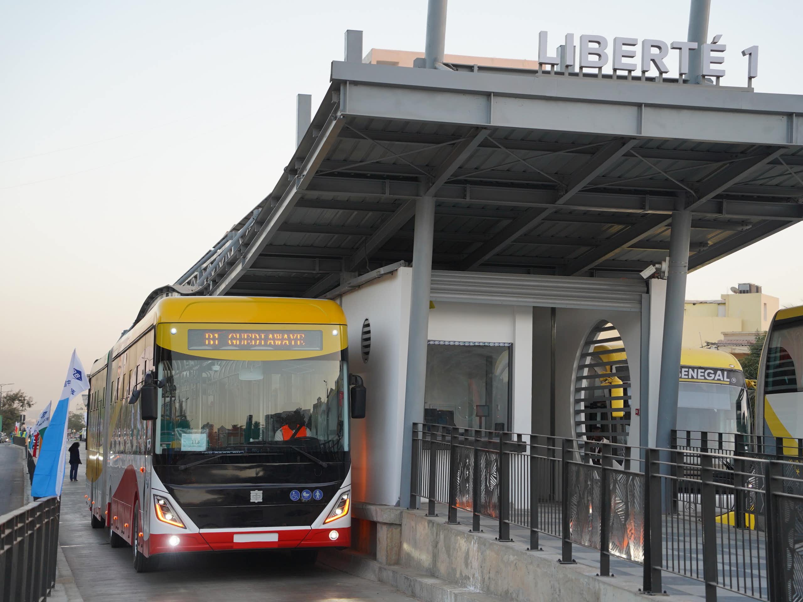 A red and yellow electric bus parked under a smart new bus shelter