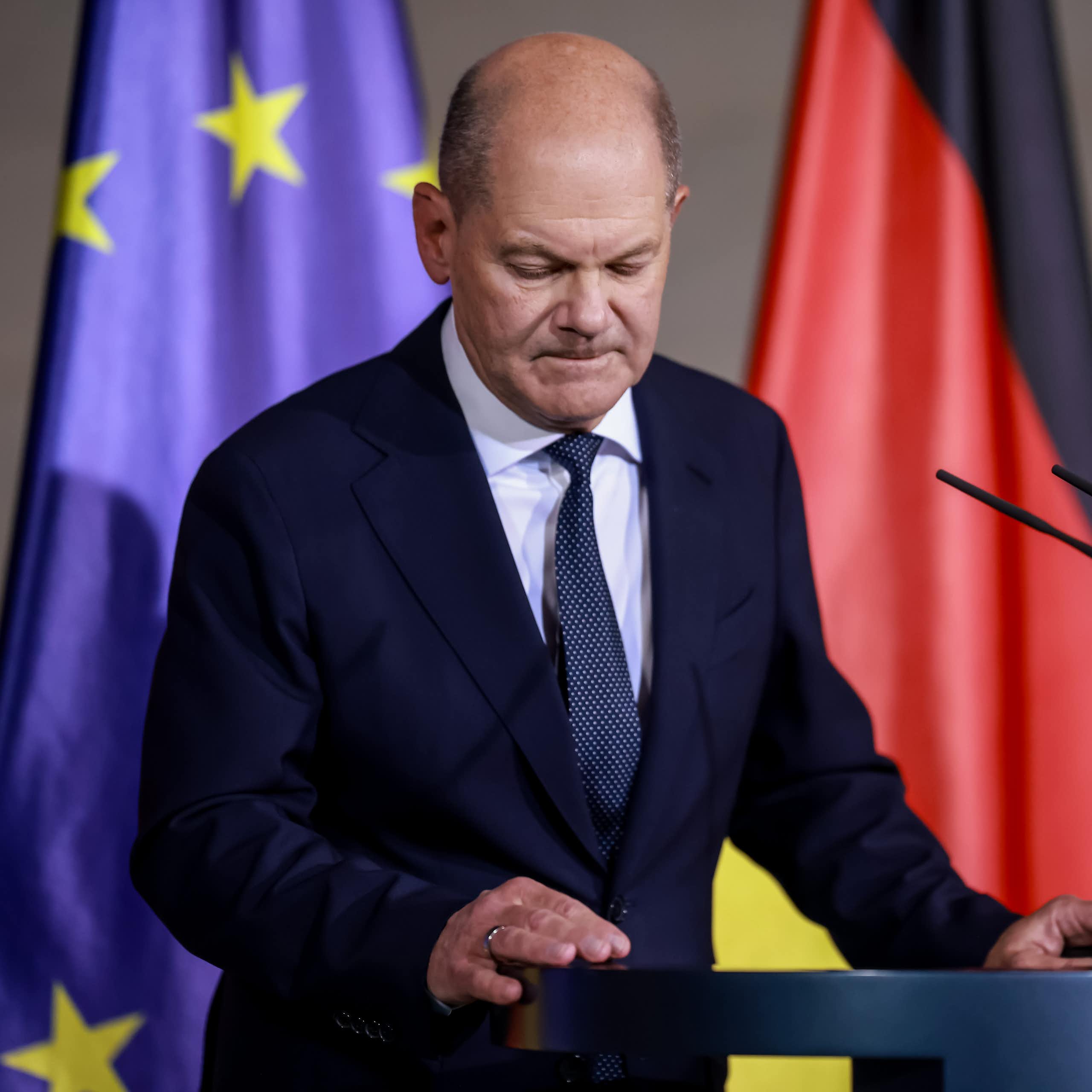 Olaf Scholz stands at a podium in front of German and EU flags