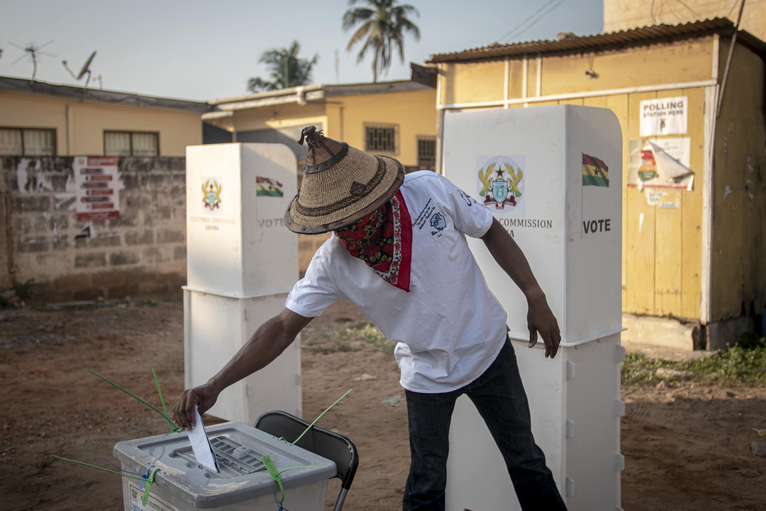 A man in a hat puts a folded paper in a ballot box