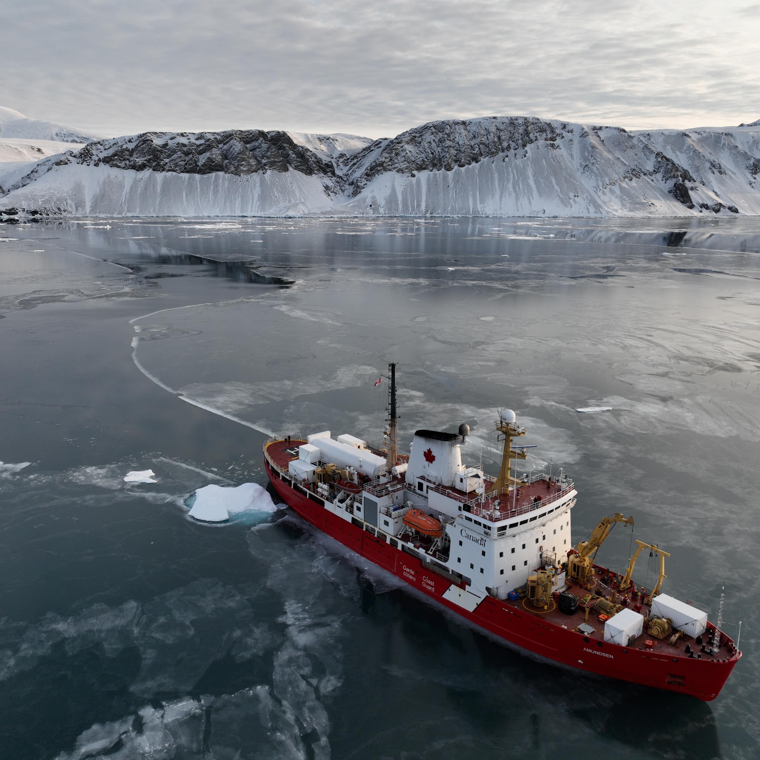 An icebreaker sails away from an icy cliff.
