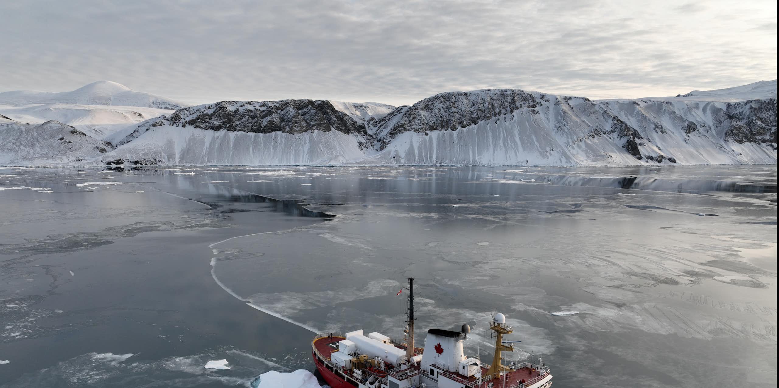 An icebreaker sails away from an icy cliff.