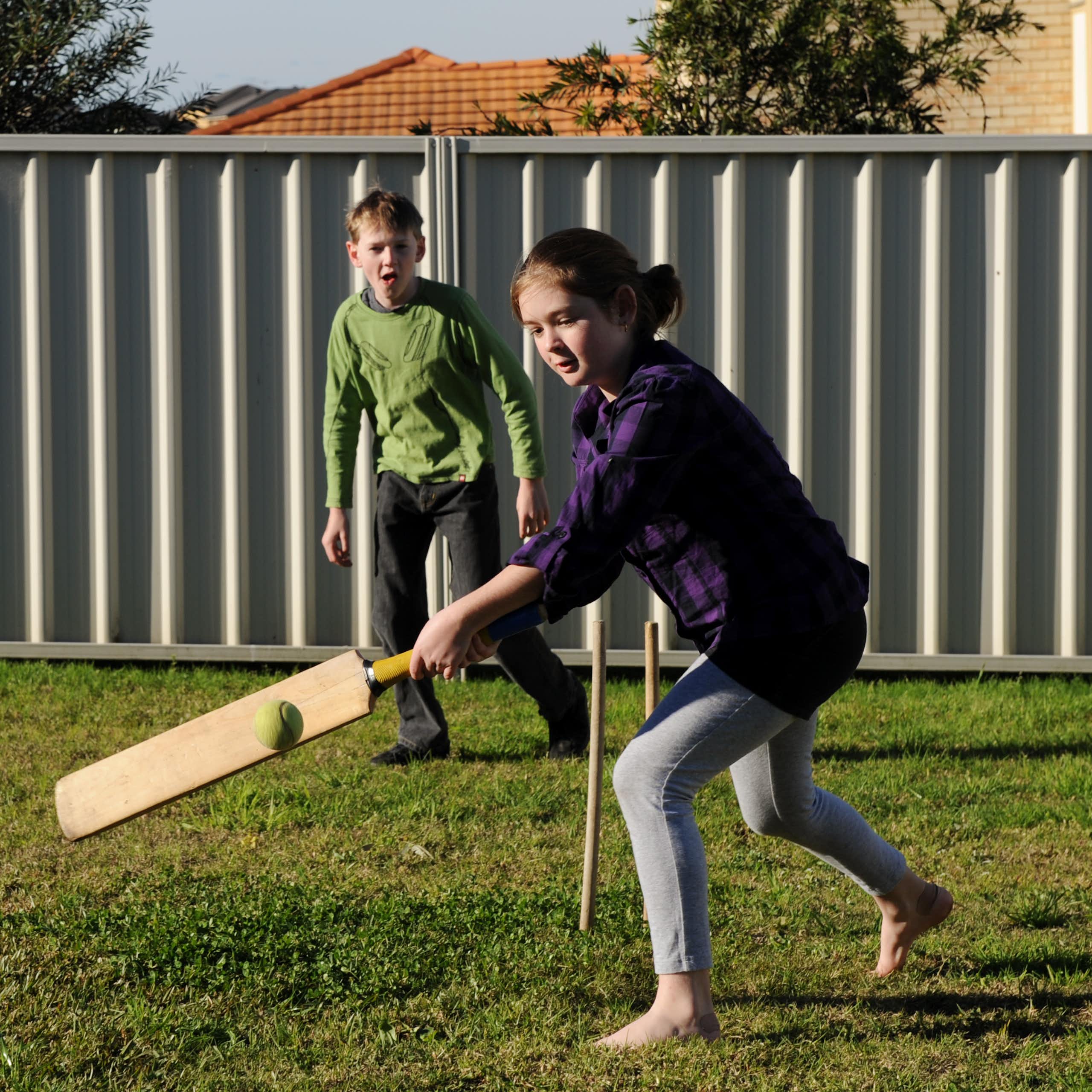 A young boy and girl play backyard cricket