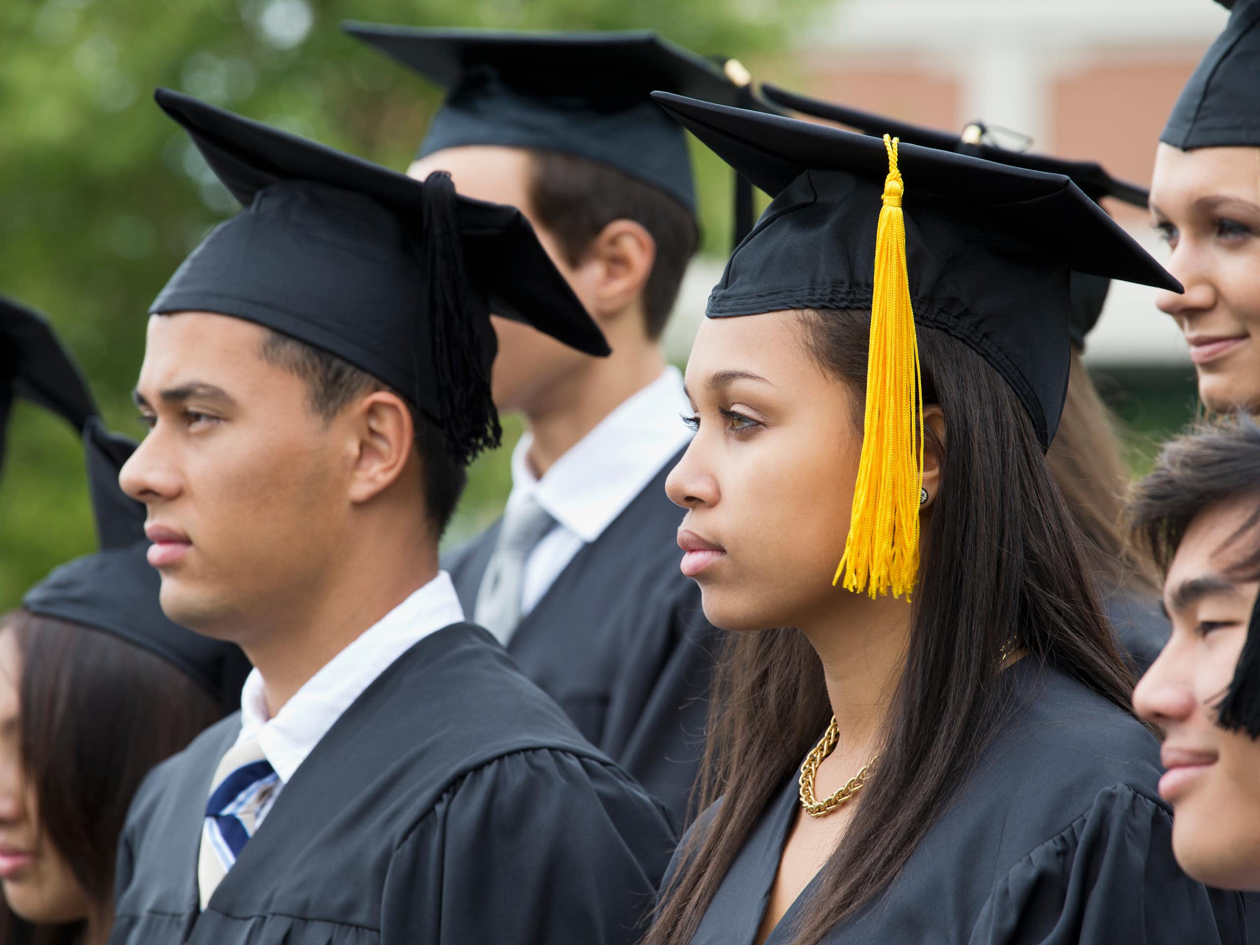 Several college students wearing caps and gowns look on at their graduation ceremony.
