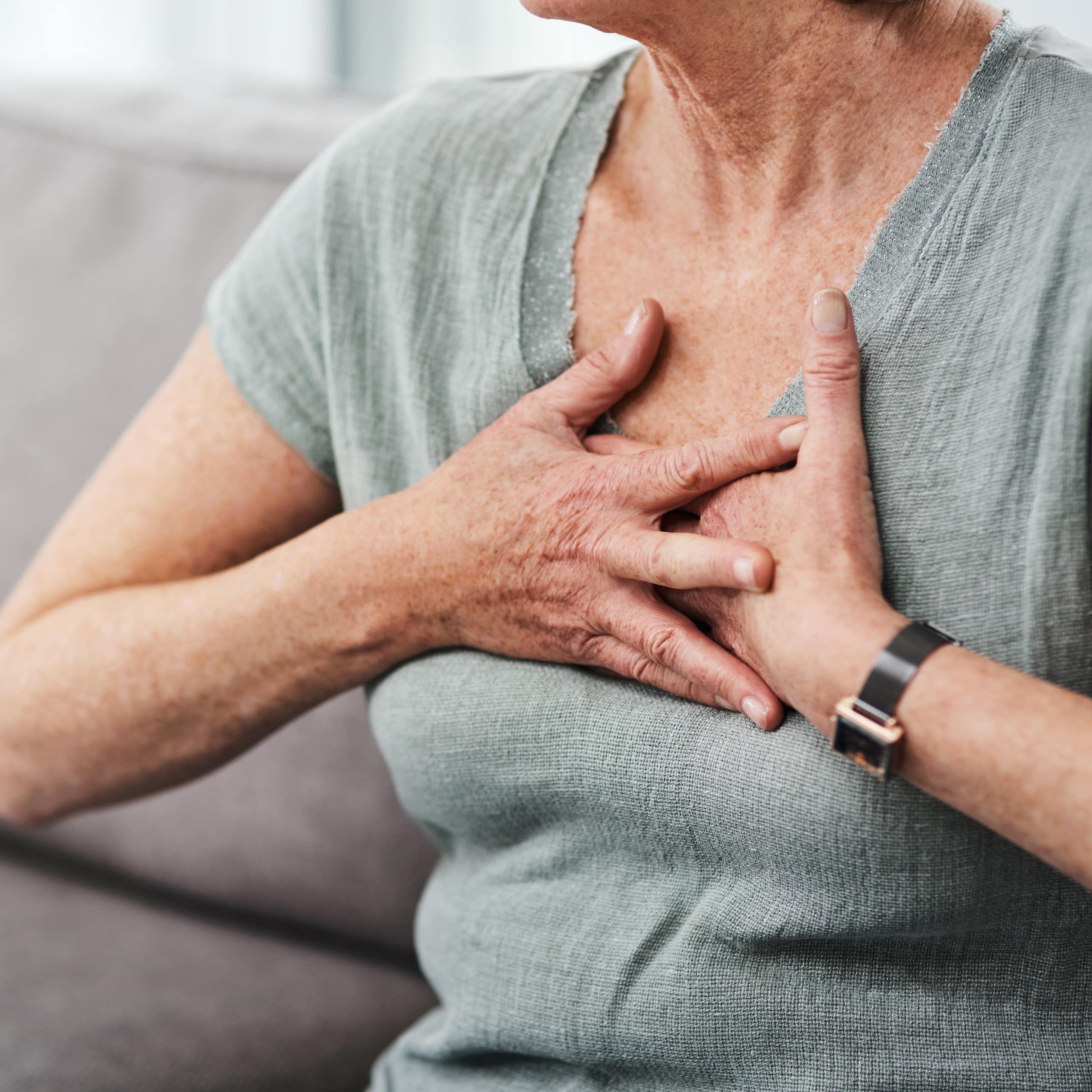 A woman with her face cropped out of frame sitting on a sofa holding her hands to her chest