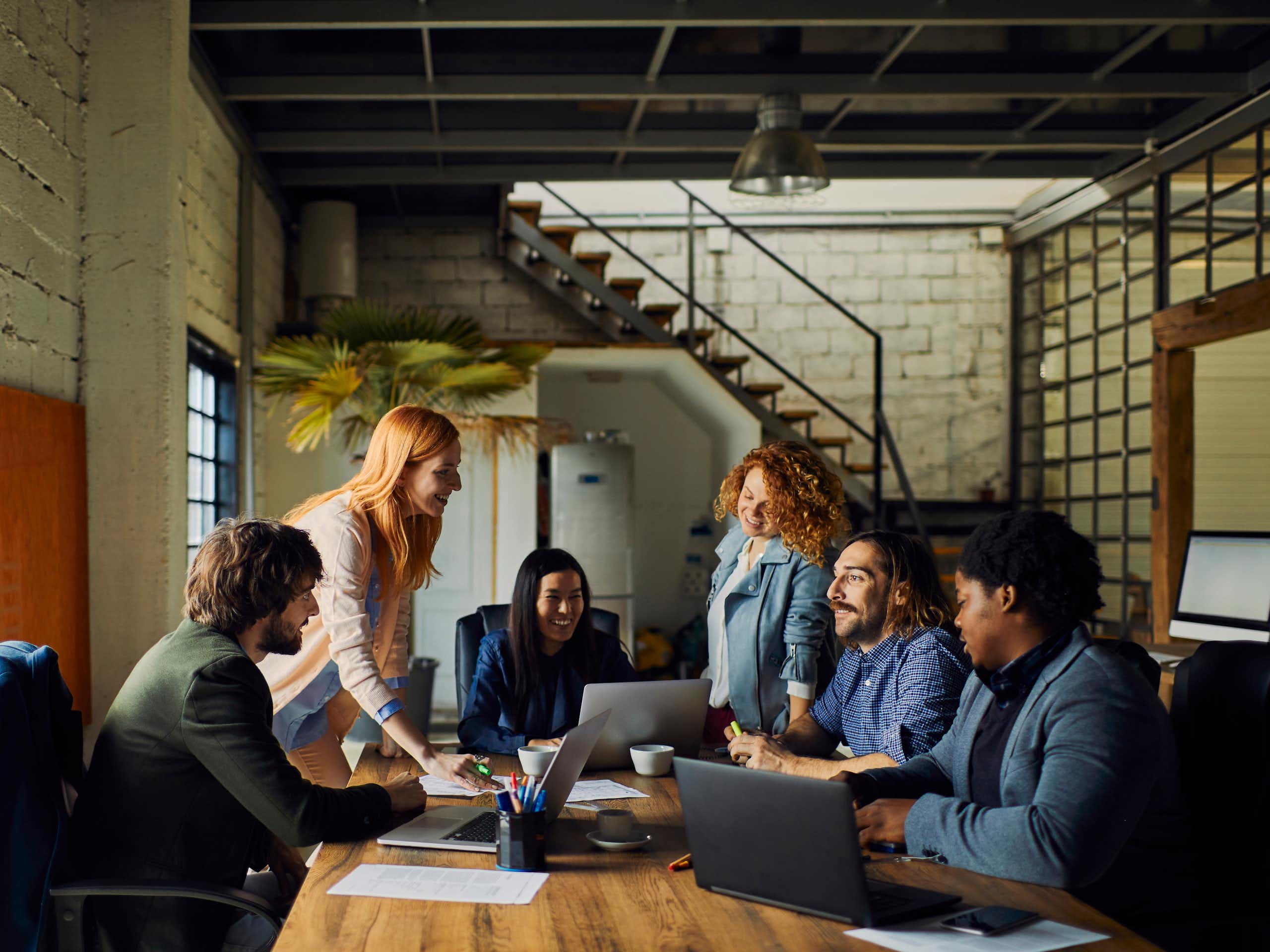 A group of people, all from diverse racial backgrounds, sit around a conference table having a conversation