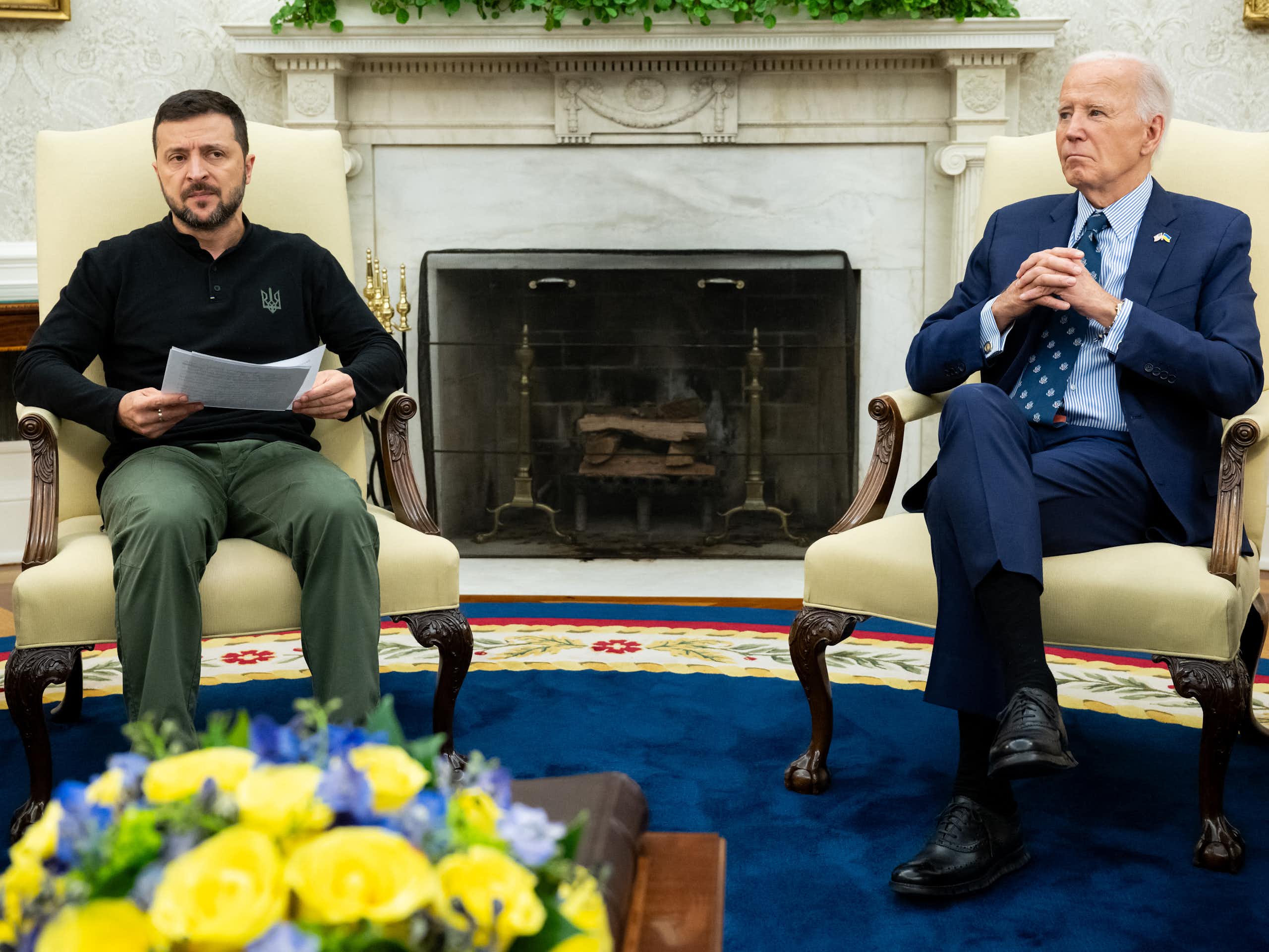 Two men, one in a suit, the other in a polo-neck shirt, sit on ornate chairs.