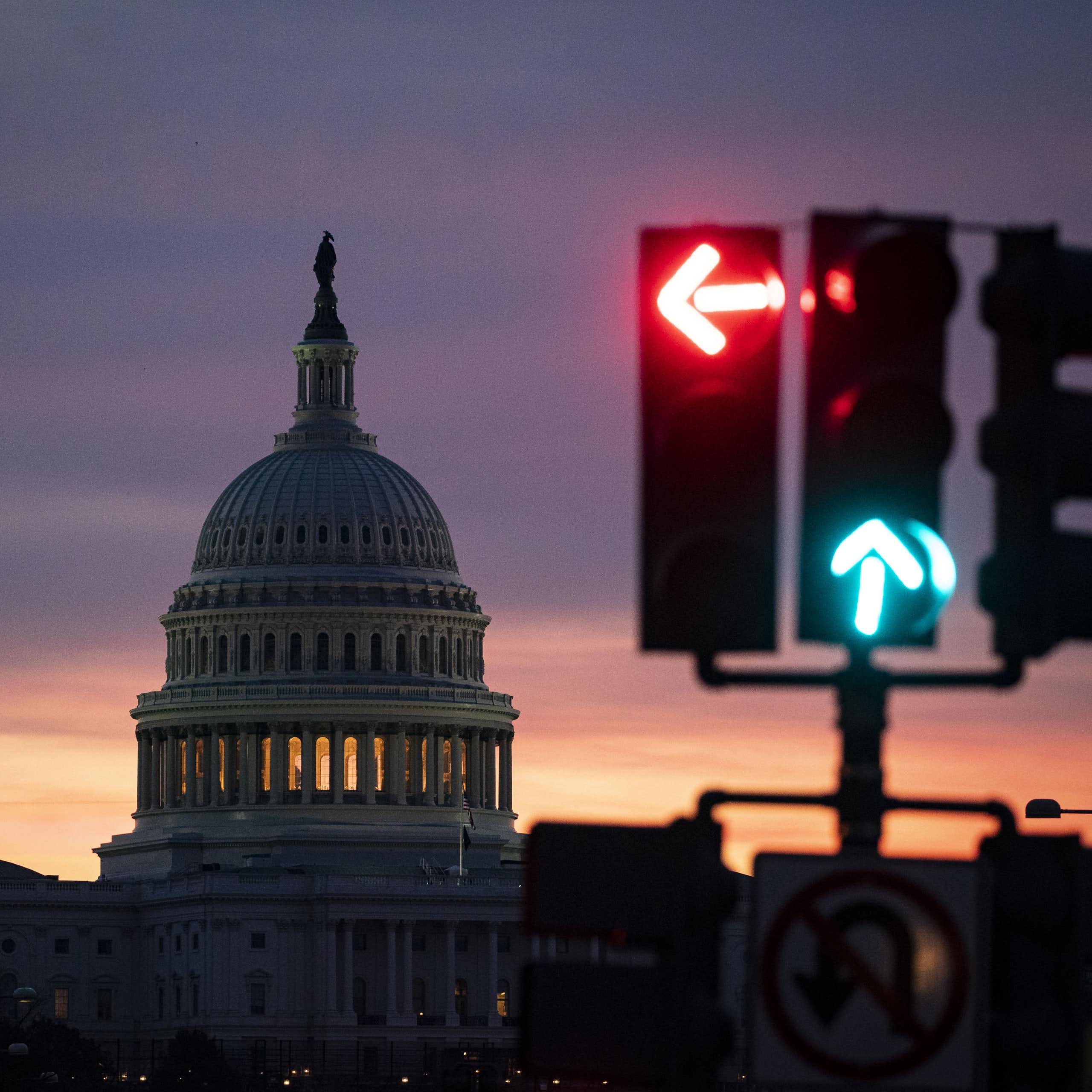 A dark sky with a large white building that has a spire on it, behind a traffic light.