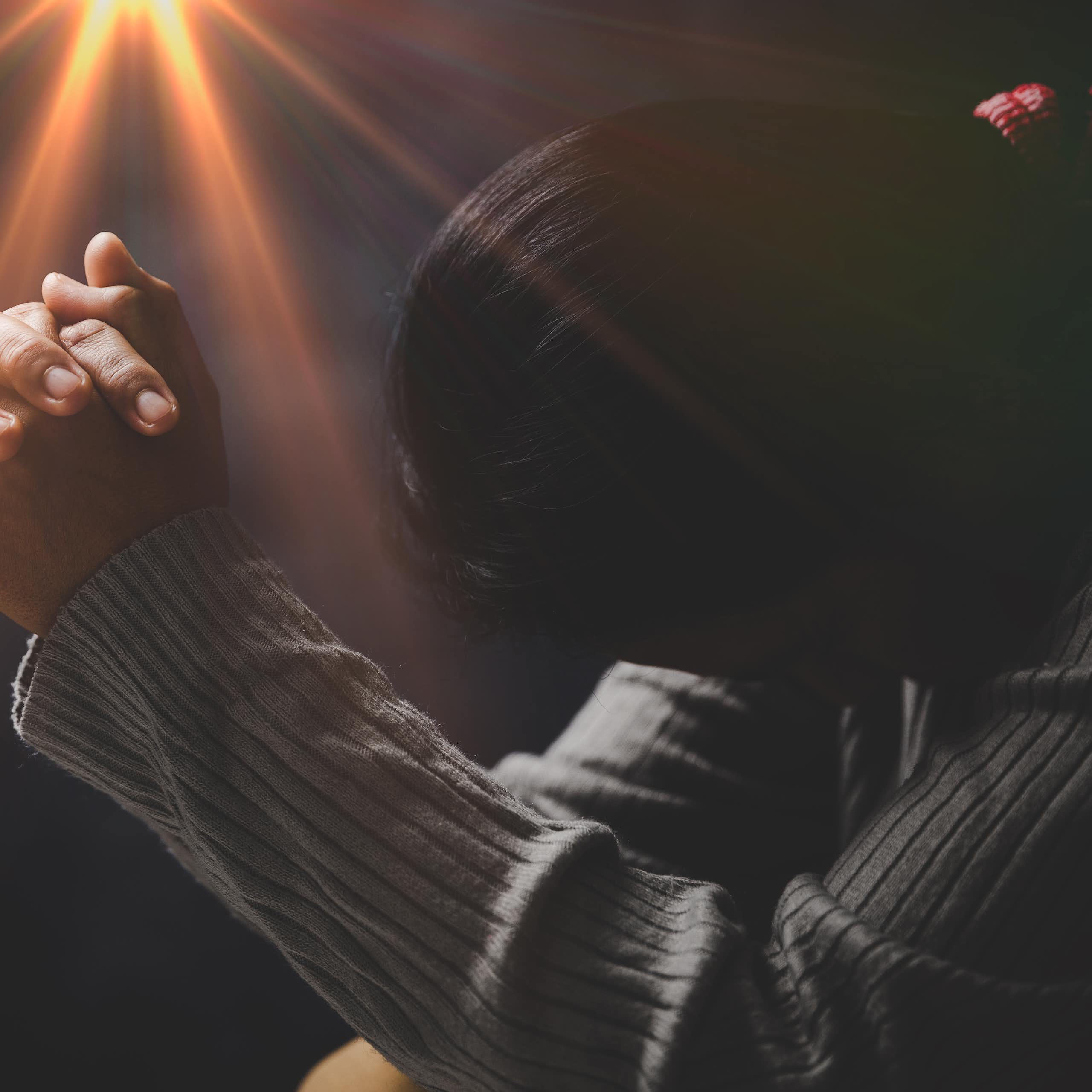 A woman with folded hands against a black background with a yellow light coming from above them