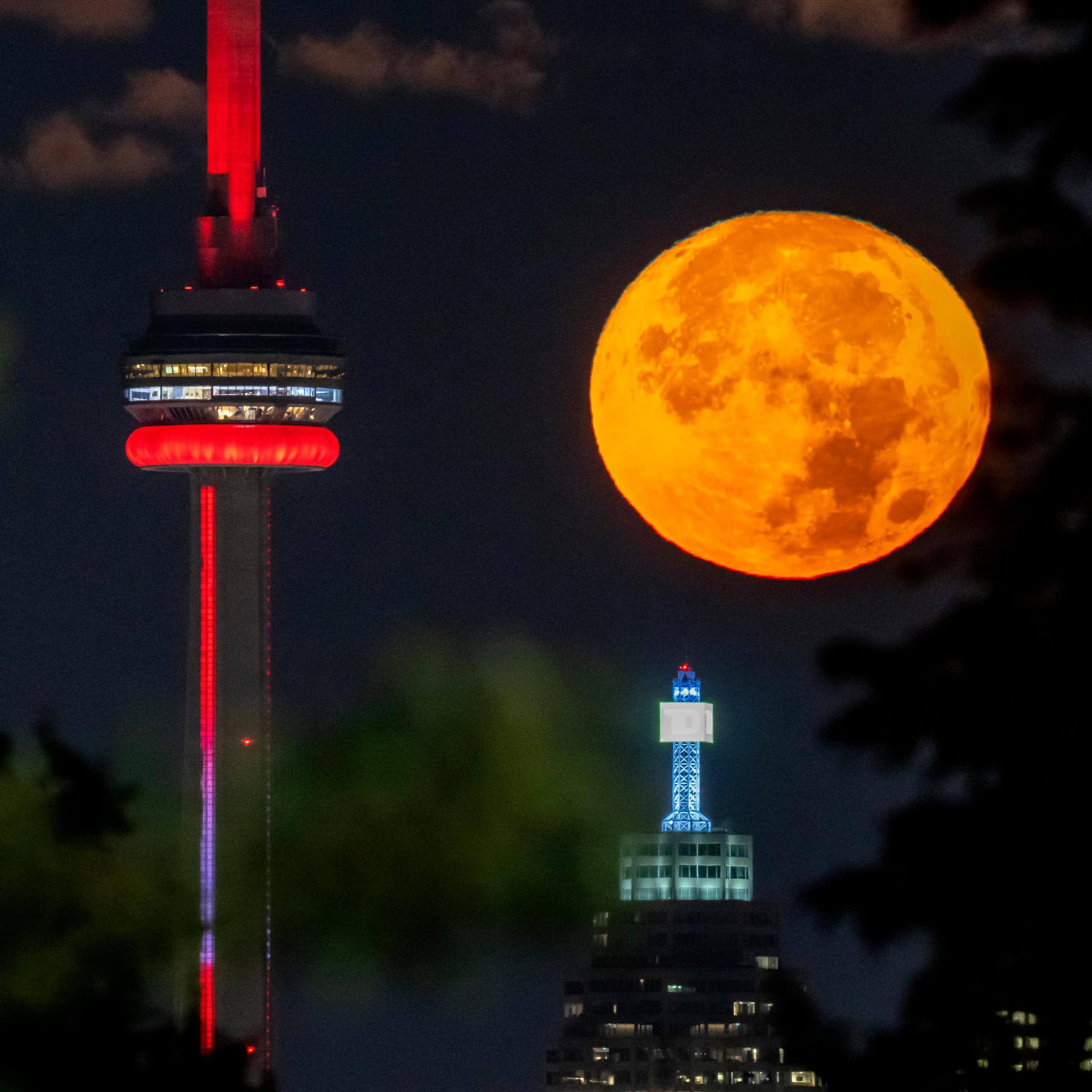 An orange moon sets behind towers at night.