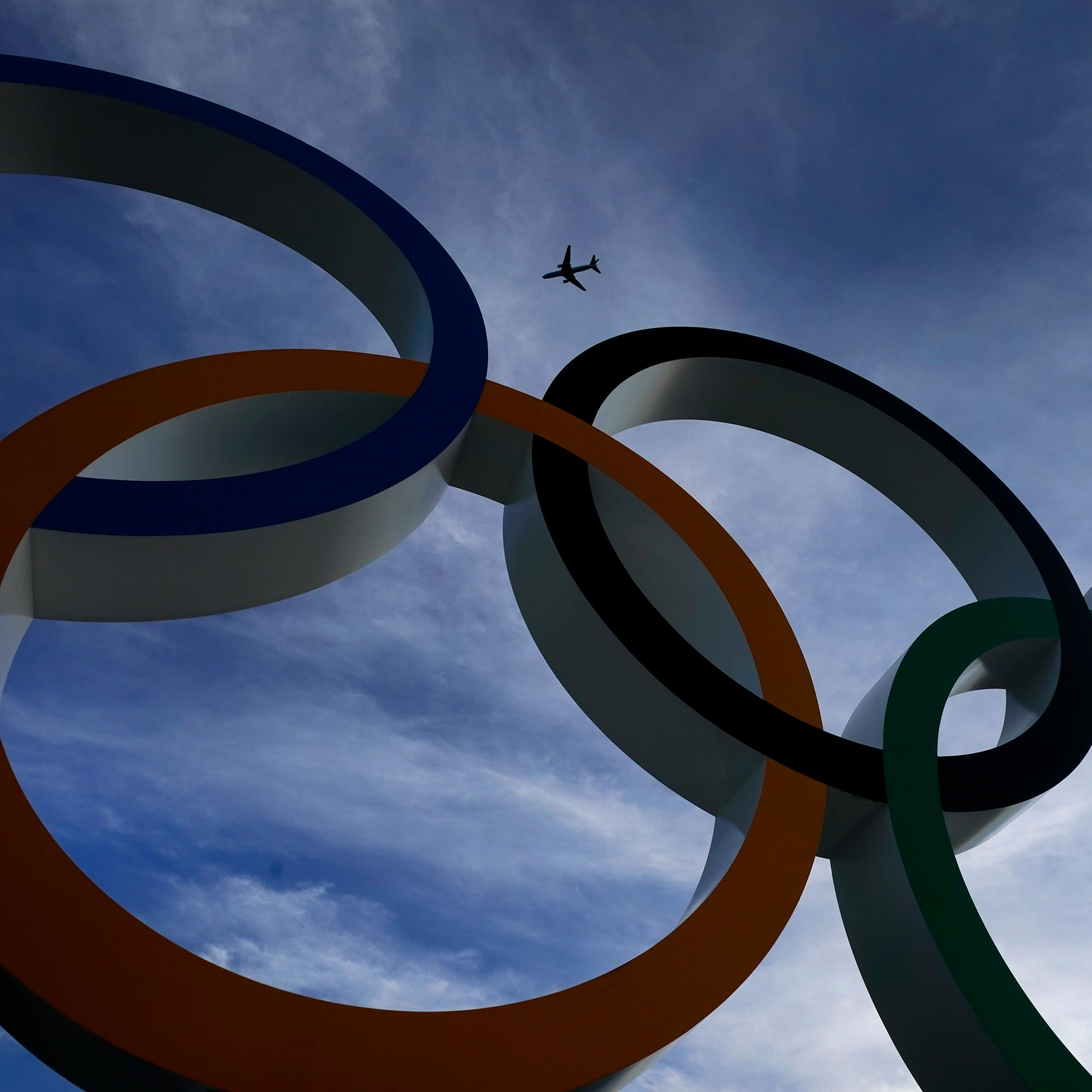 A passenger jet is seen flying over the five Olympic rings.
