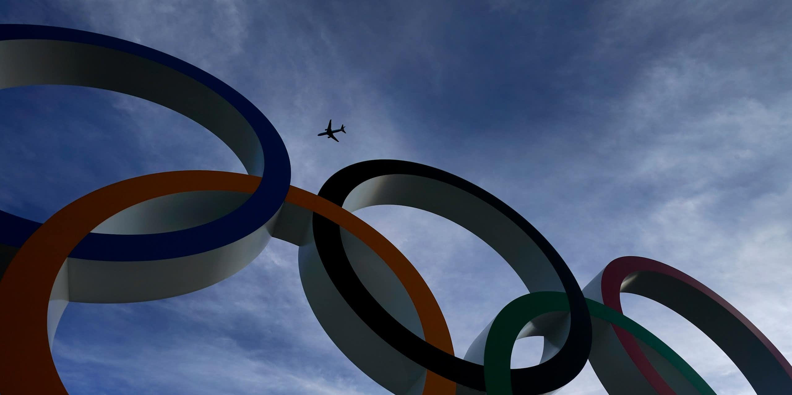 A passenger jet is seen flying over the five Olympic rings.