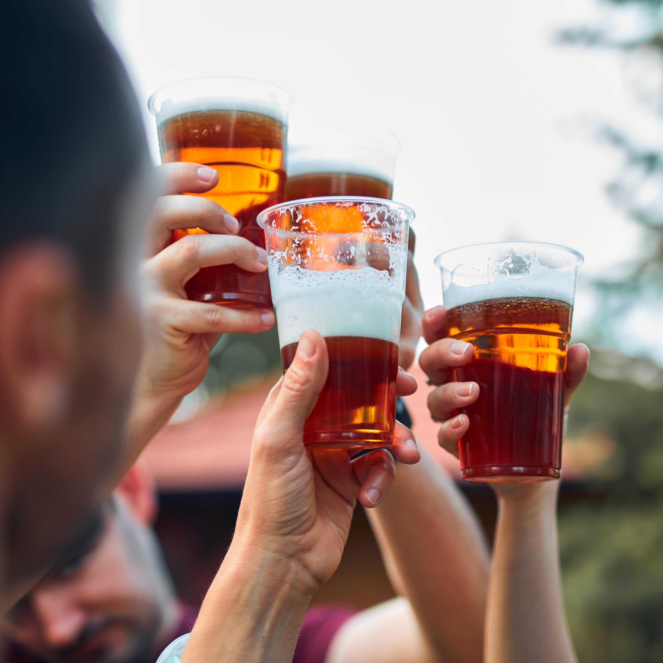 Close up of hands holding glasses of a foamy, amber-coloured beverage knocking their cups together