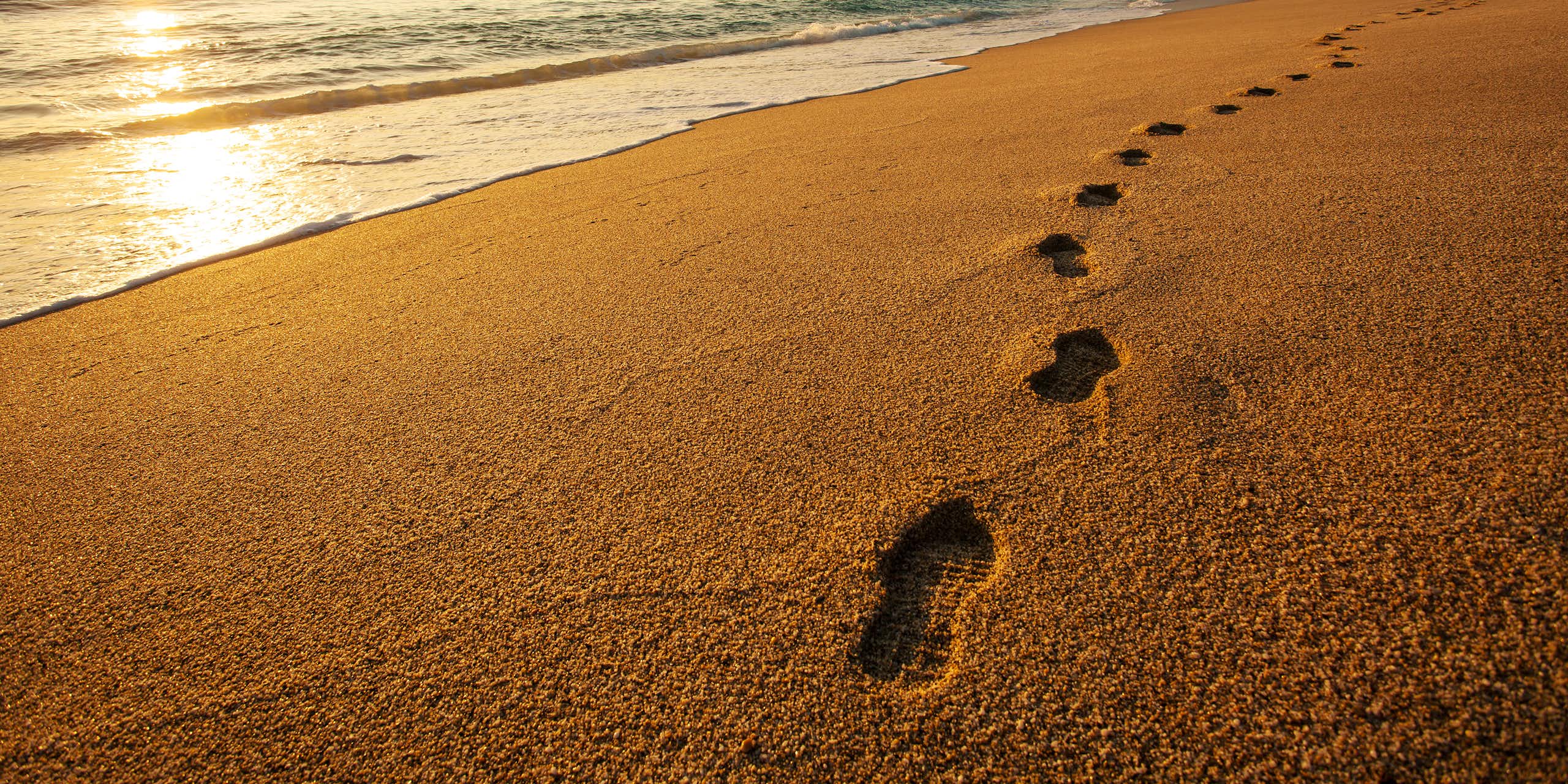A set of footprints made by someone wearing running shoes or sneakers stretches along a sandy beach