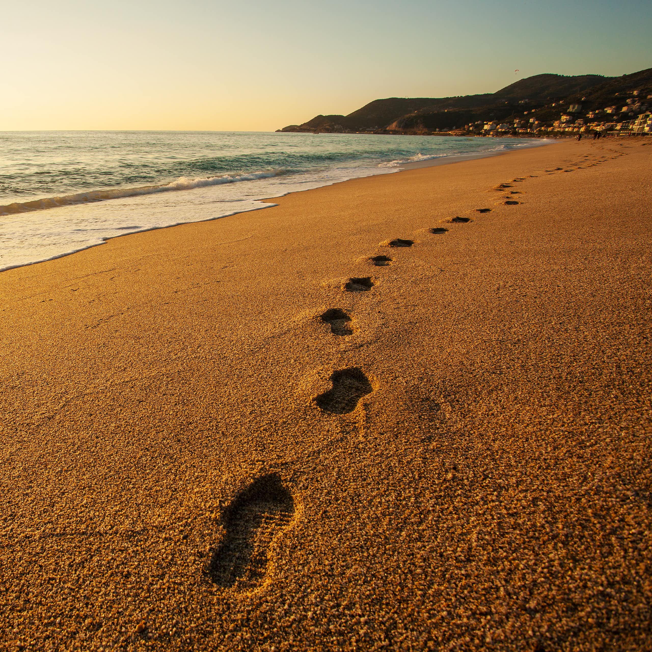 A set of footprints made by someone wearing running shoes or sneakers stretches along a sandy beach