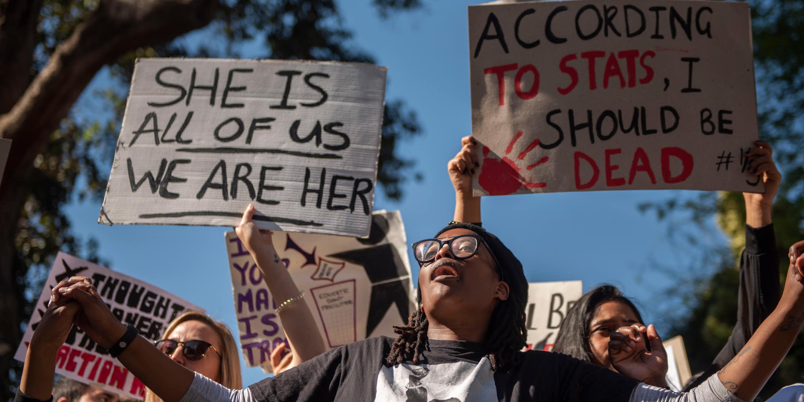 A group of protesters, some holding signs that read she is all of us we are her and according to stats I should be dead