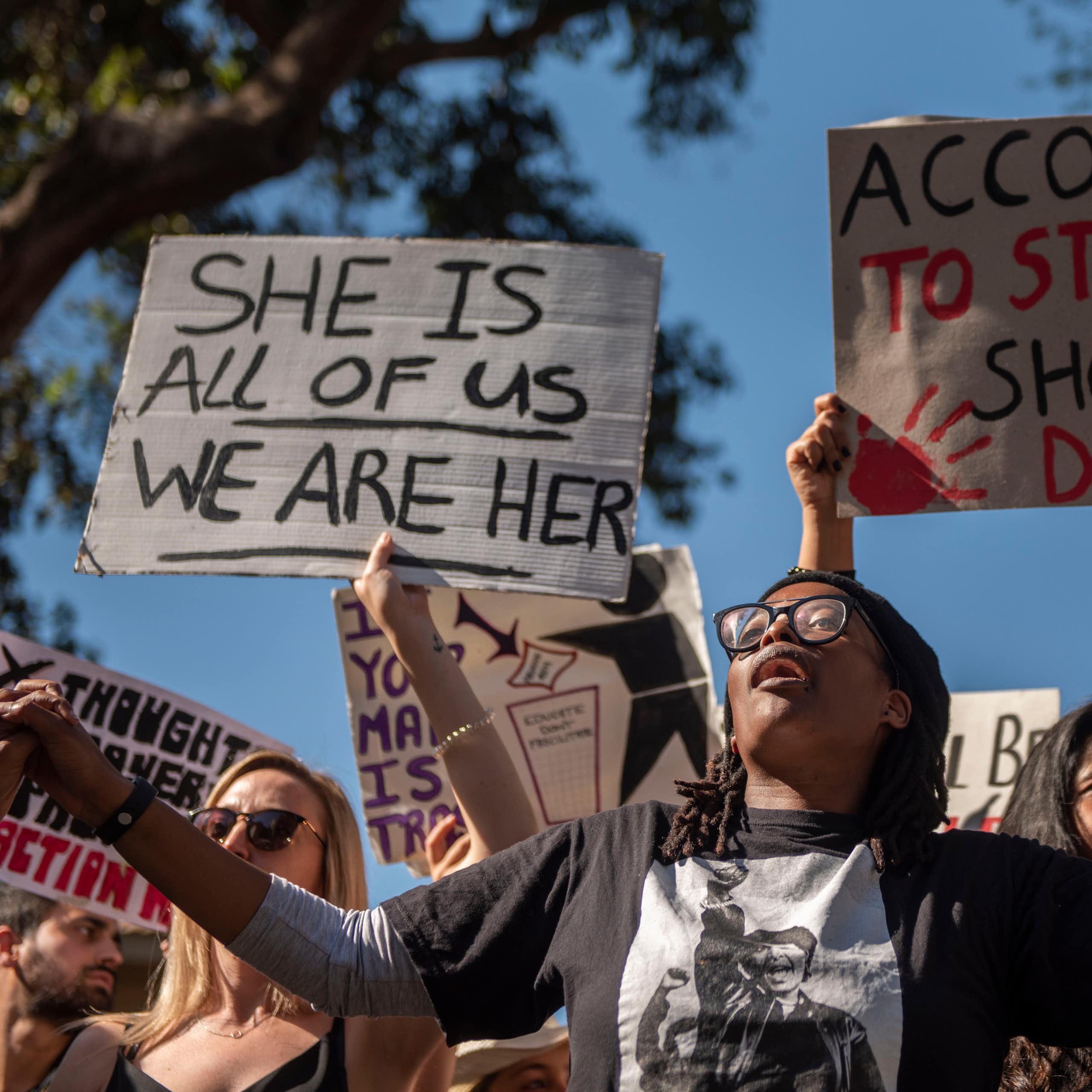 A group of protesters, some holding signs that read she is all of us we are her and according to stats I should be dead