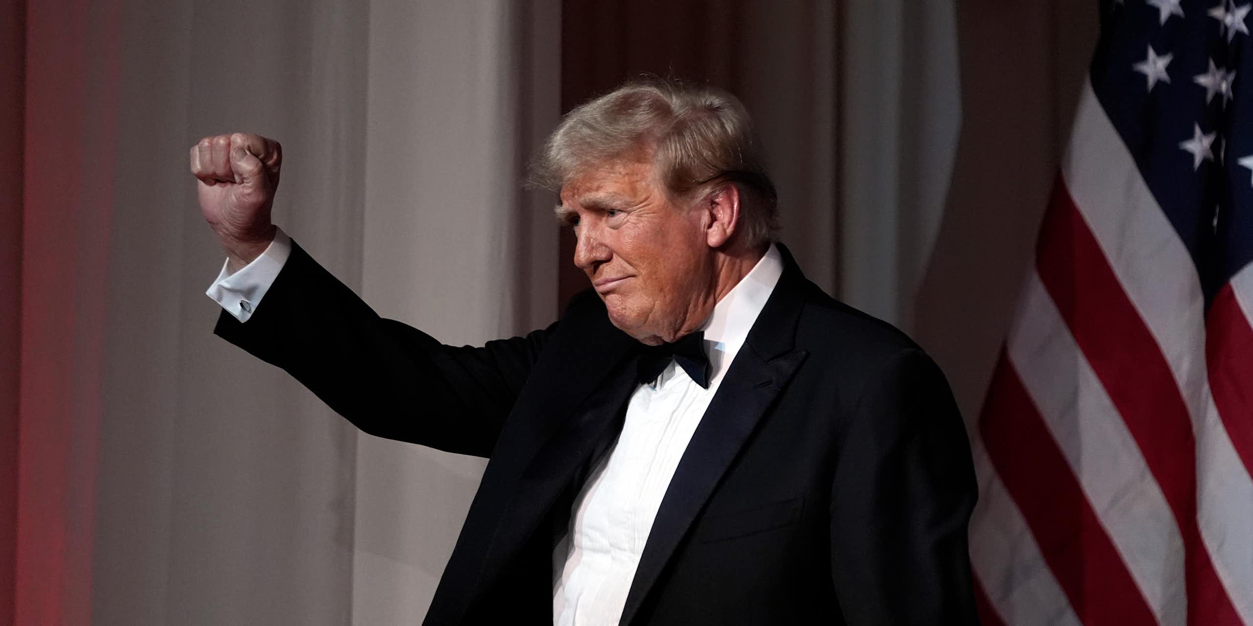 A rotund man with grey-blond hair in a tuxedo raises his fist.