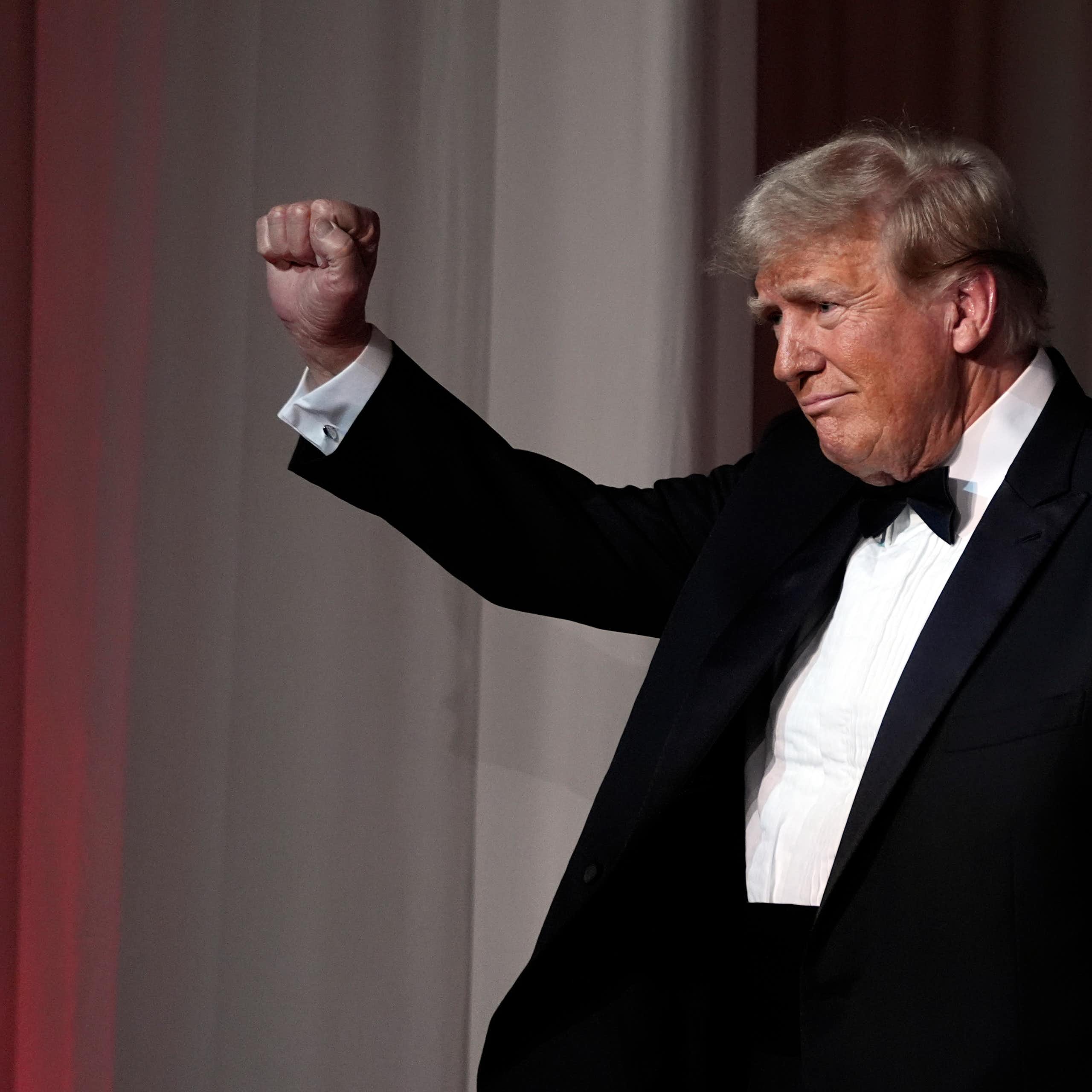 A rotund man with grey-blond hair in a tuxedo raises his fist.