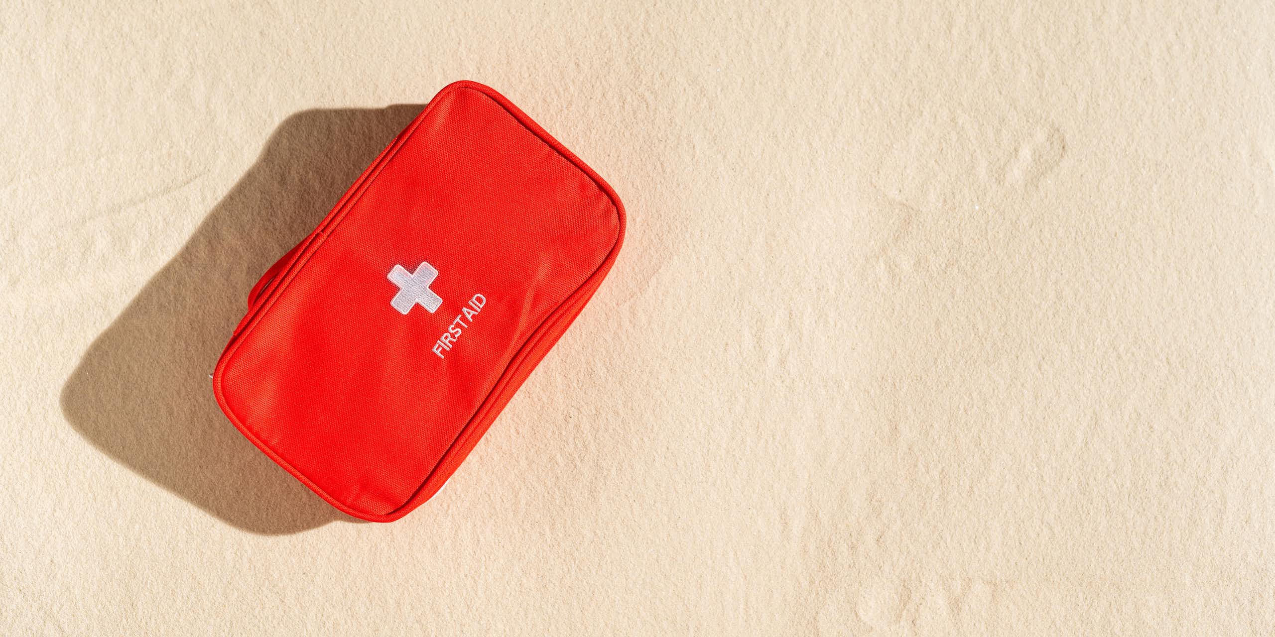 red first aid kit sits on sand