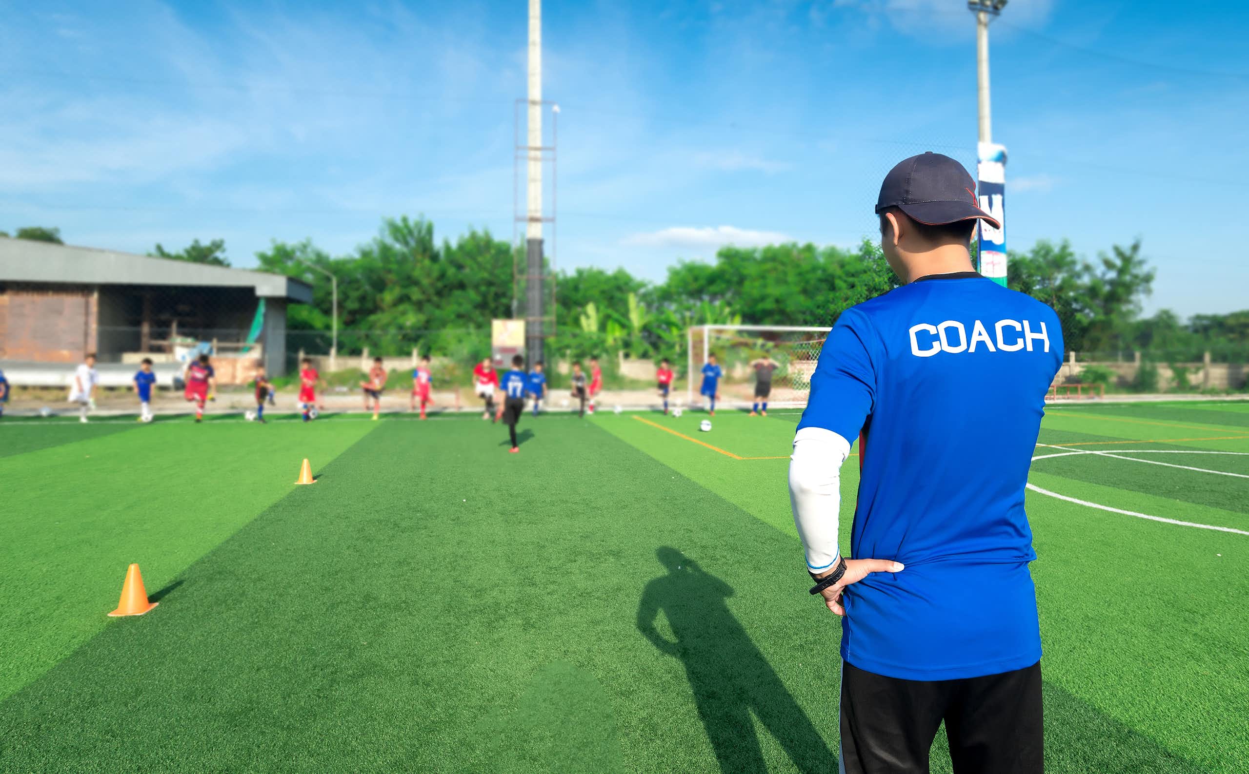 A sports coach looks on as his team trains