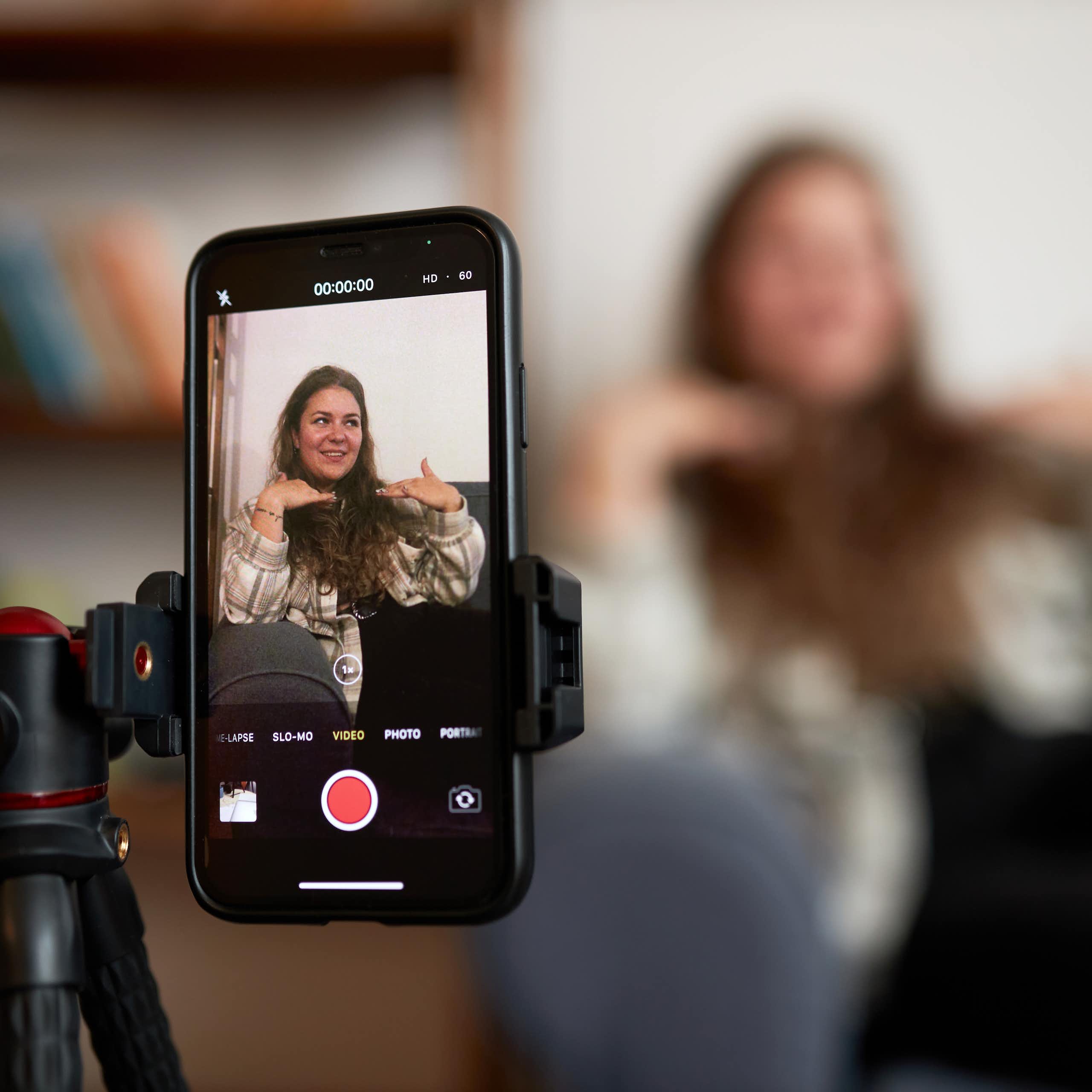 Close up of a phone on a tripod filming a woman sitting on a couch