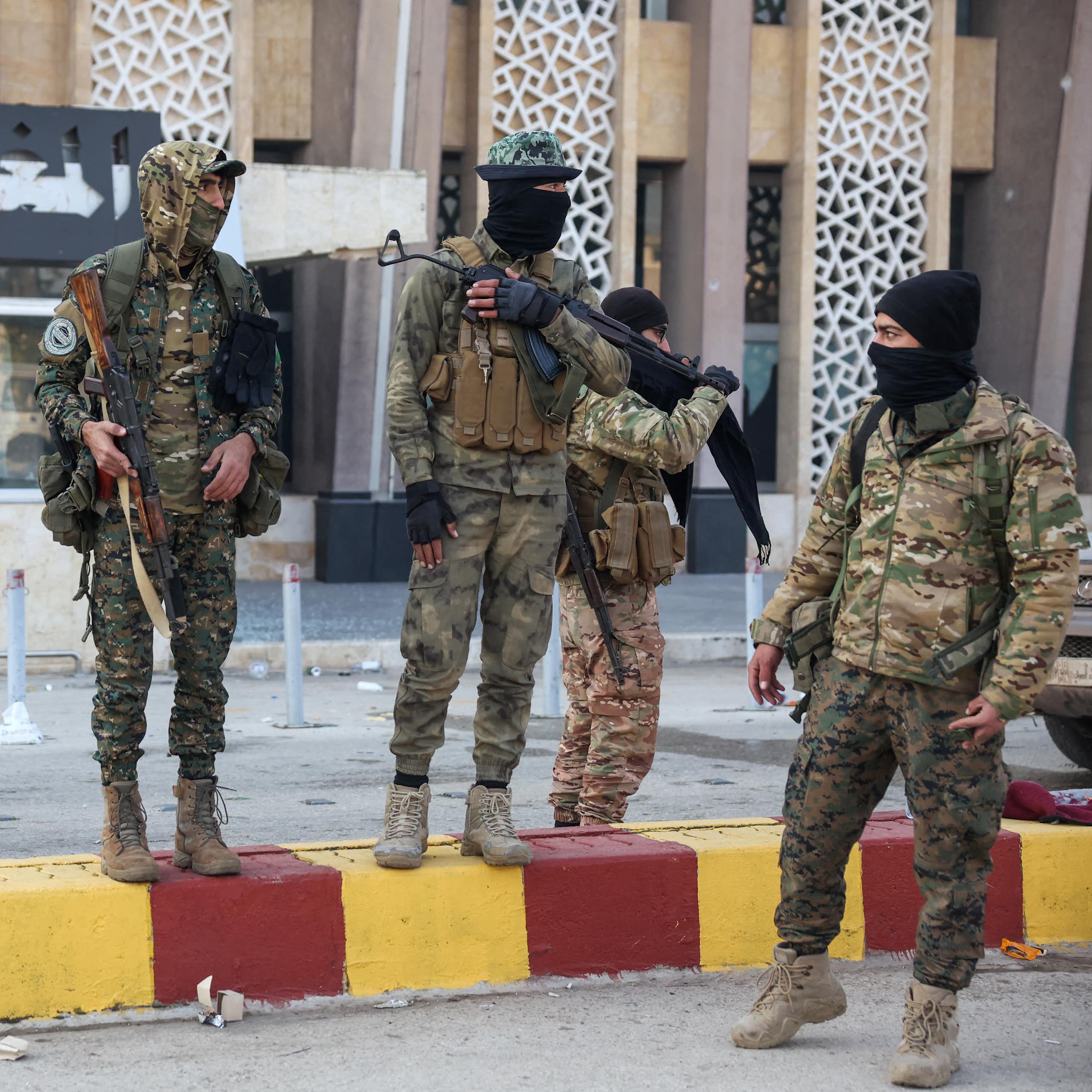 A group of men in army fatigues stand around holding guns.