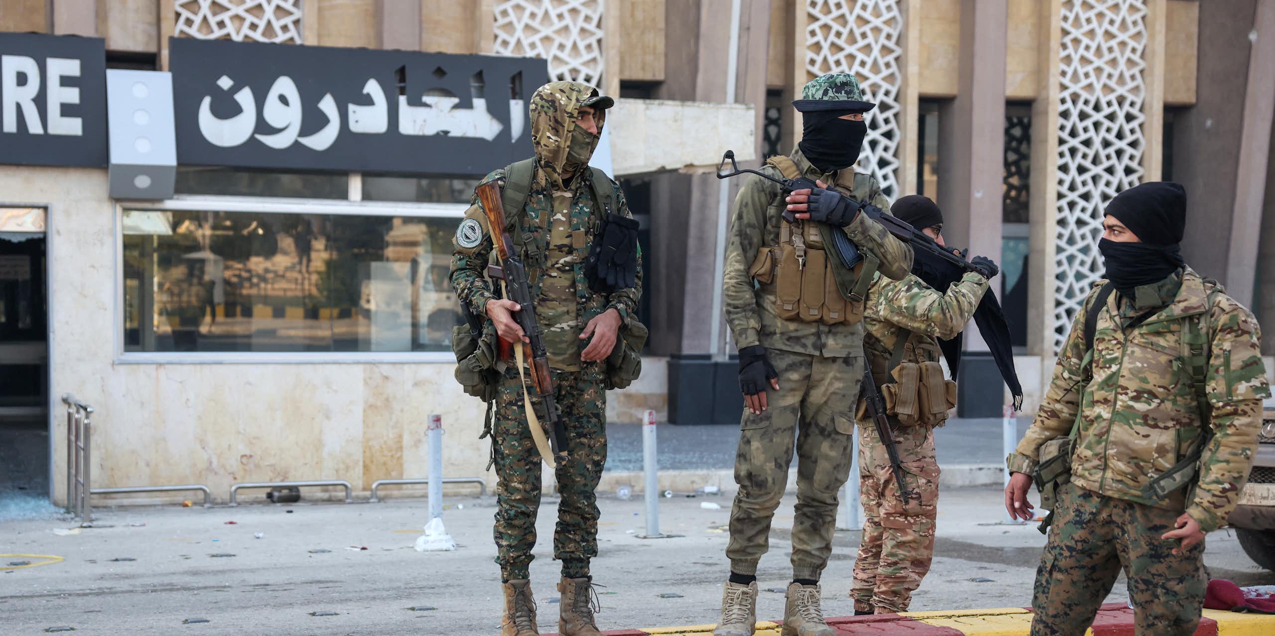 A group of men in army fatigues stand around holding guns.