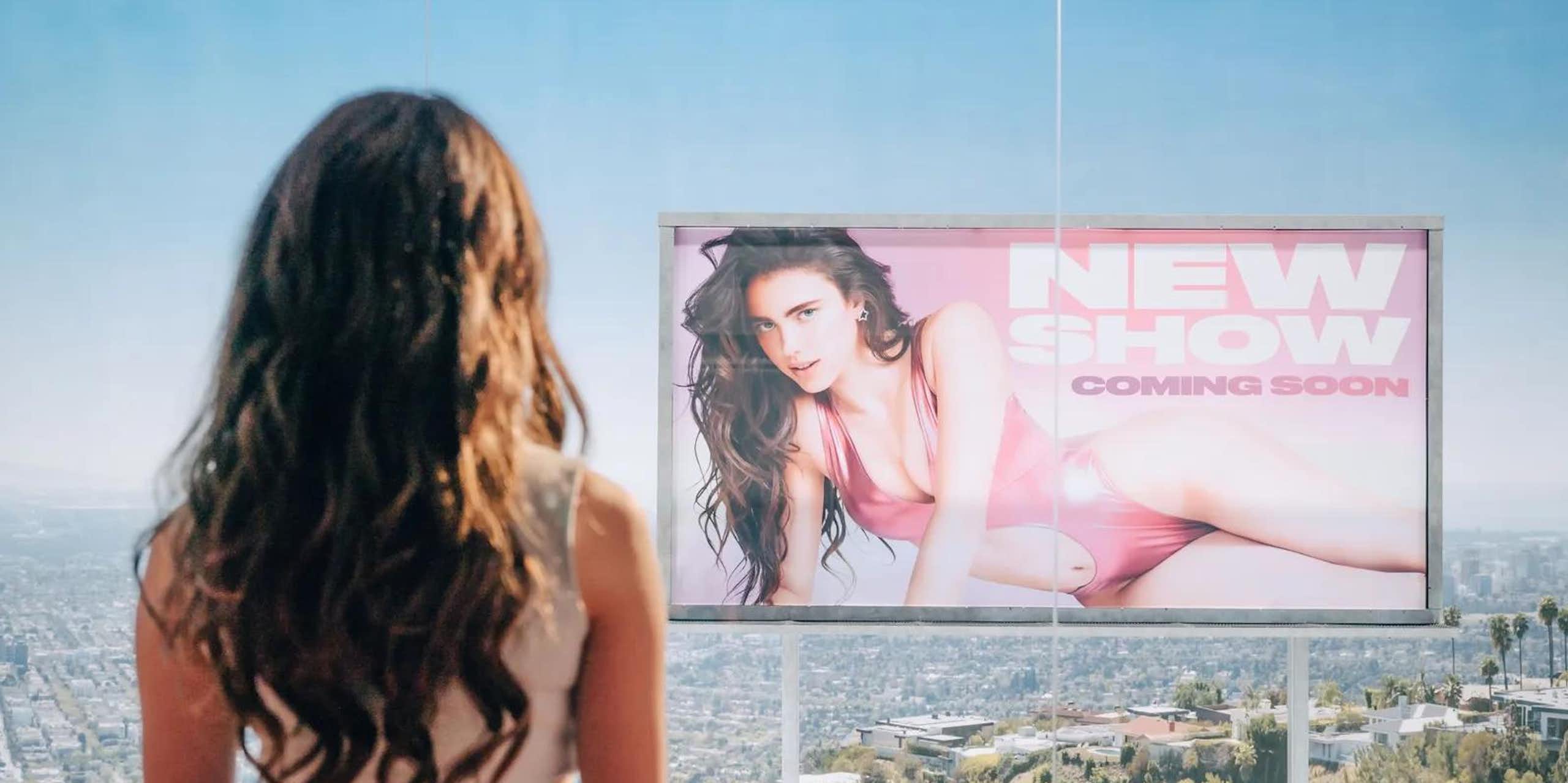 Una mujer observa un anuncio con otra mujer joven en una valla publicitaria. 