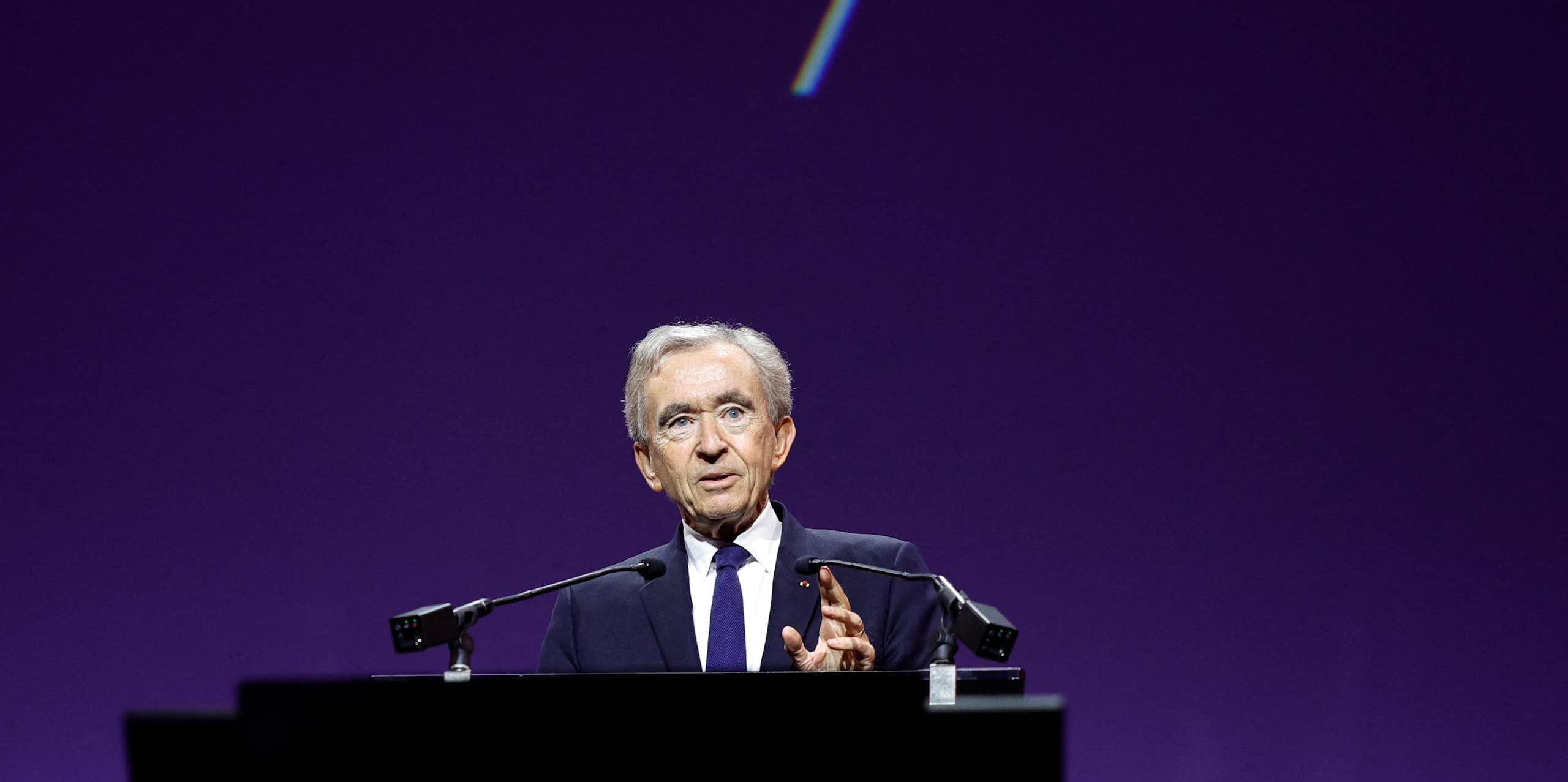 Bernard Arnault speaks at a lectern in front of a purple background.