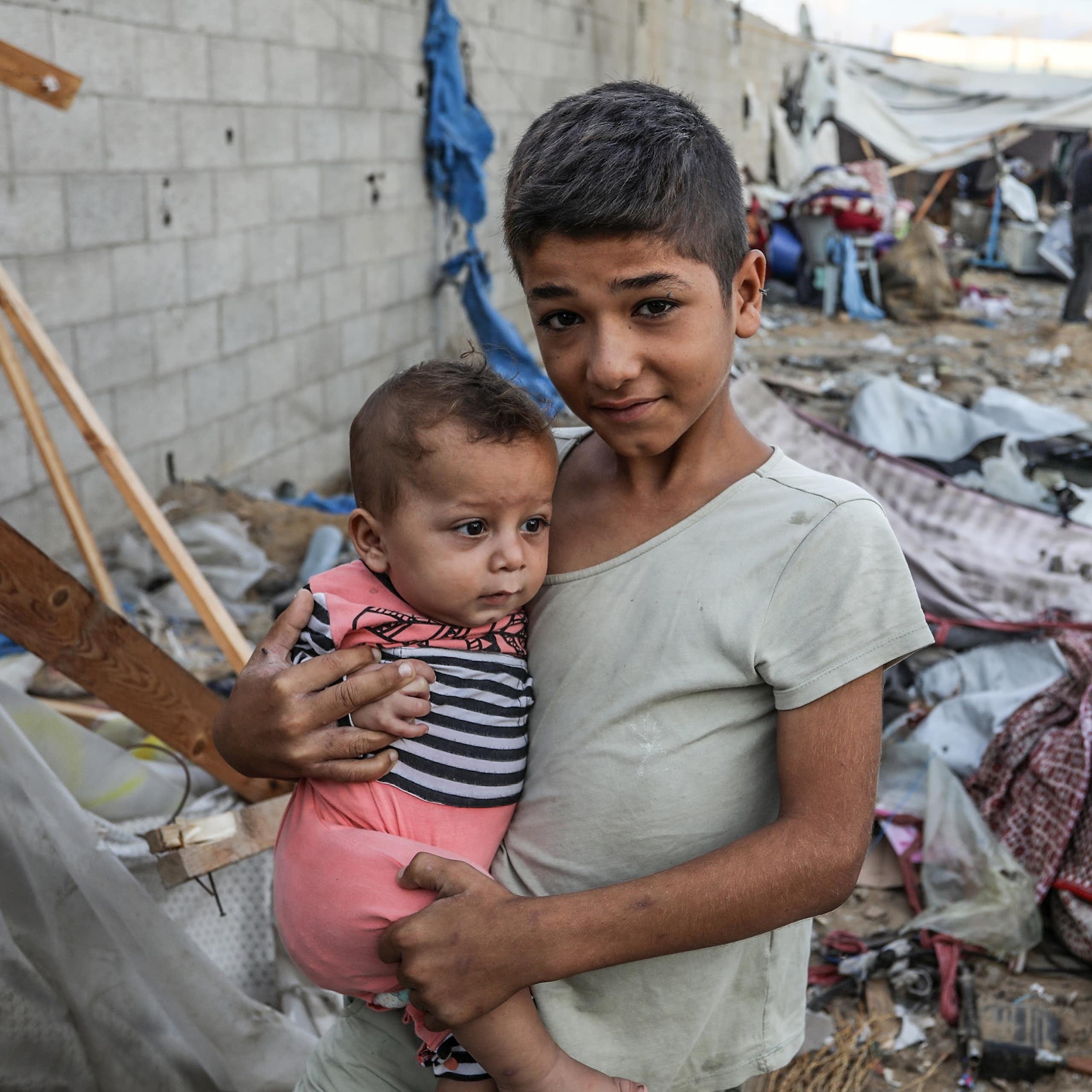 Un jeune garçon tient une enfant dans ses bras parmi les décombres.