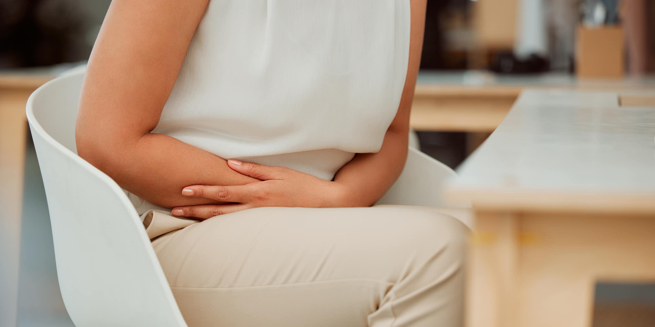 A person, seen from the neck down, clutches their arms across their lower stomach while sitting