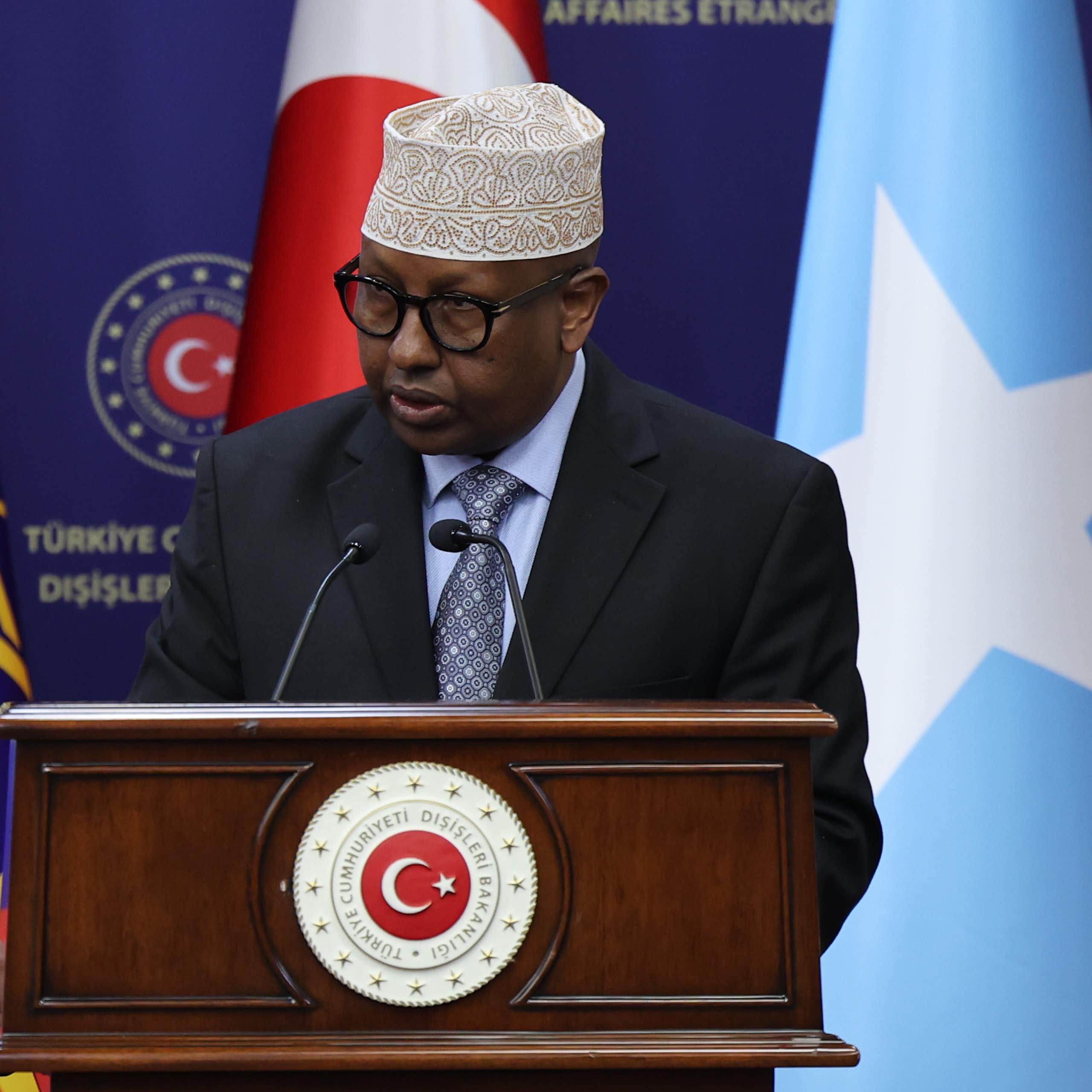 A man speaking into a microphone with three flags behind him