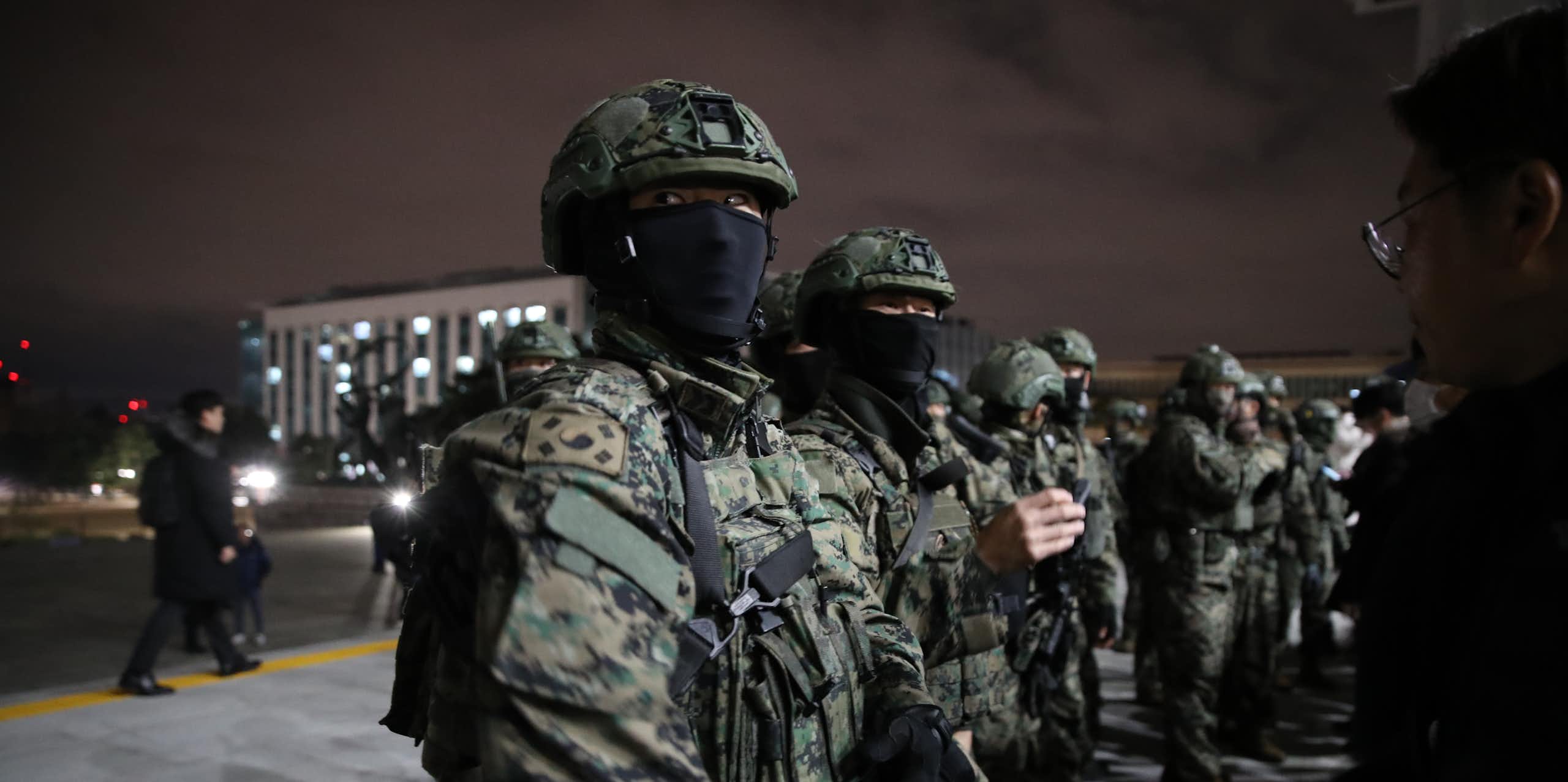 Fatigue-clad soldiers with masks covering their face stand outside a large building.