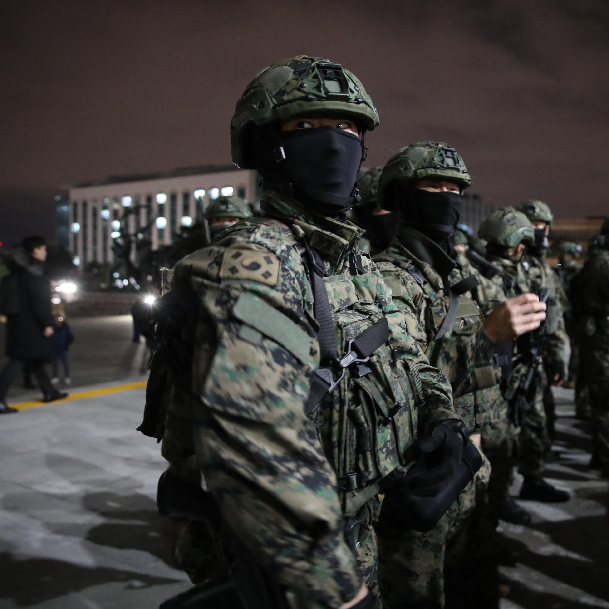 Fatigue-clad soldiers with masks covering their face stand outside a large building.