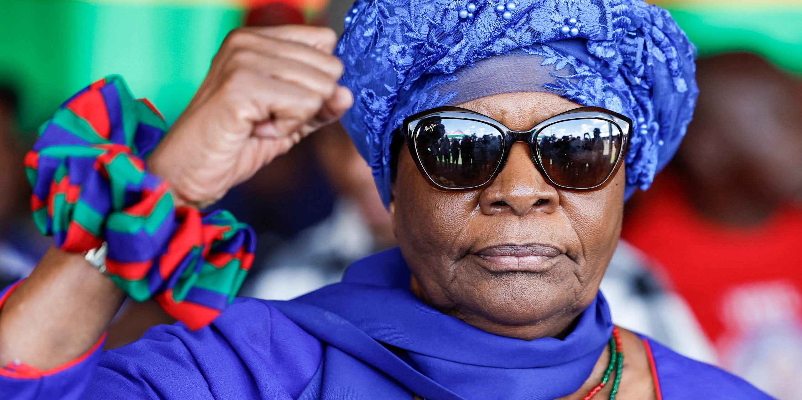 A woman wearing a turban and sunglasses raises her right hand in a black power salute