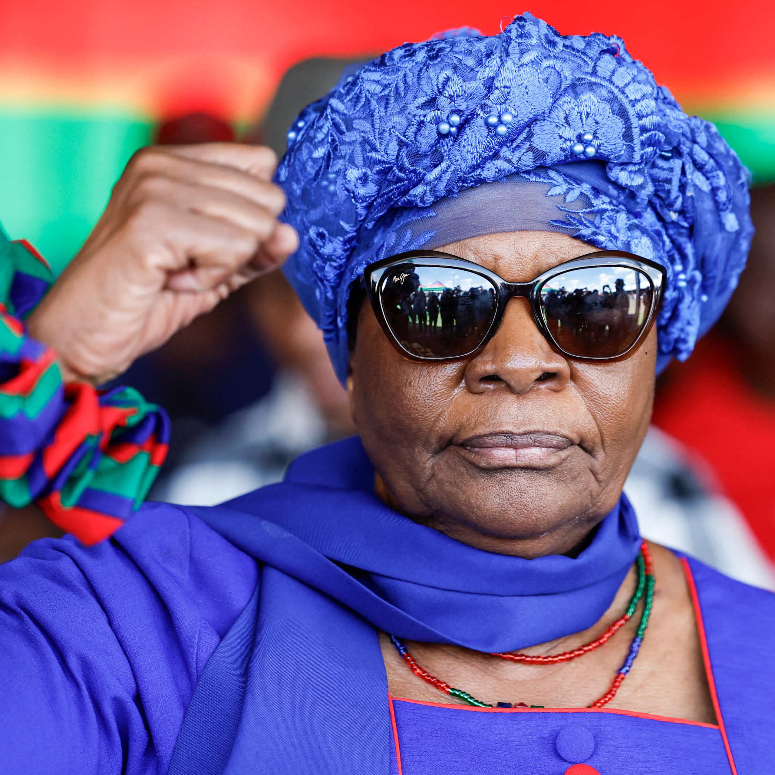 A woman wearing a turban and sunglasses raises her right hand in a black power salute