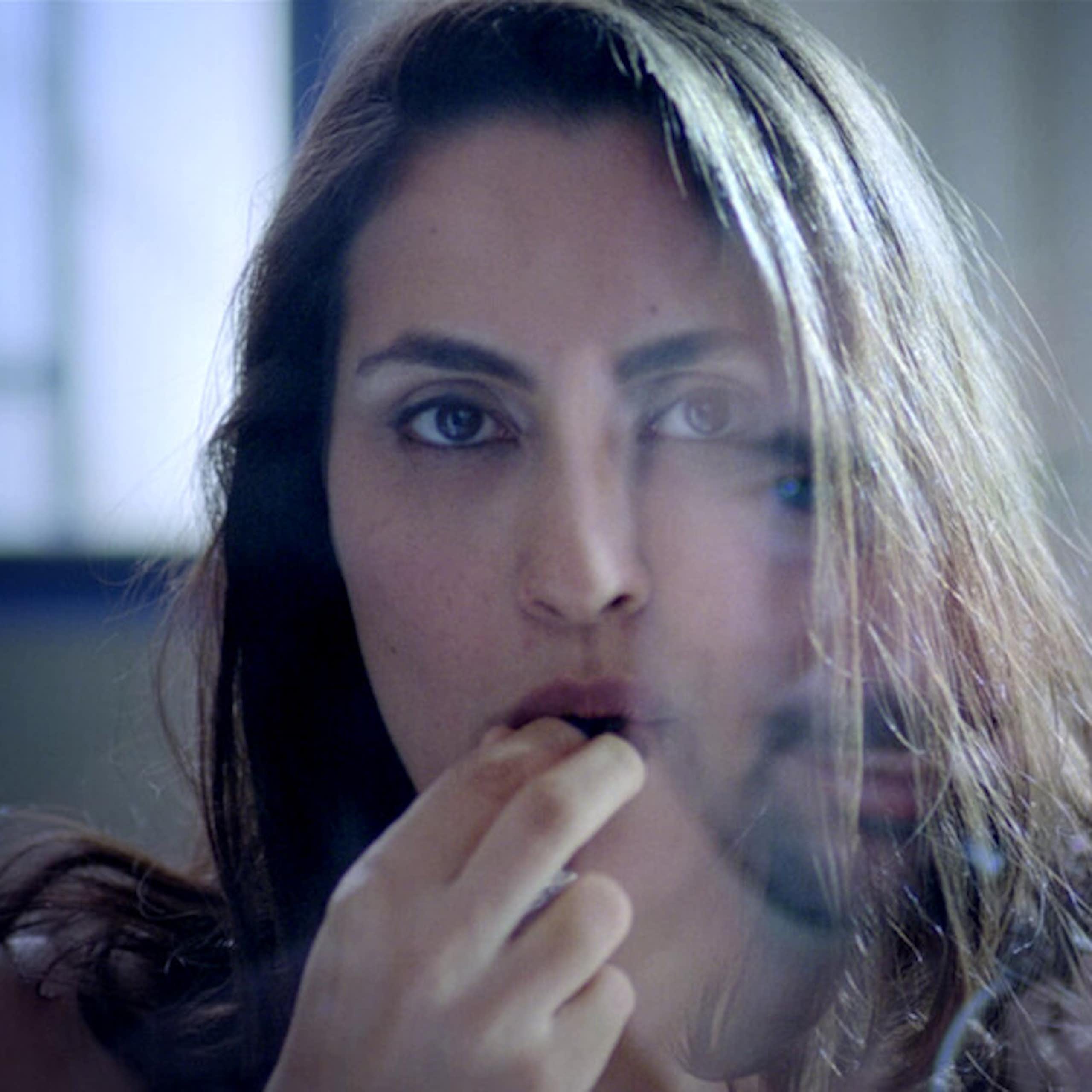 a woman looks directly into the camera as she puts a candy into her mouth. 
