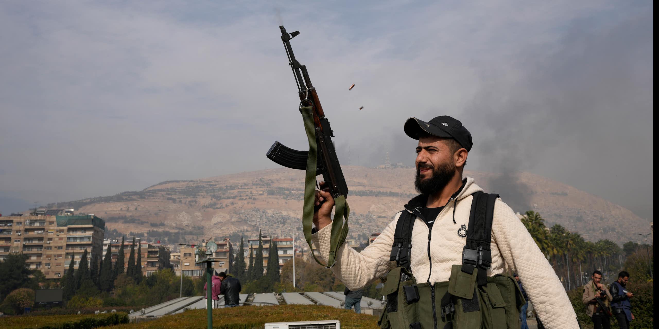 A bearded fighter smiles as he fires his AK-47 over his head.